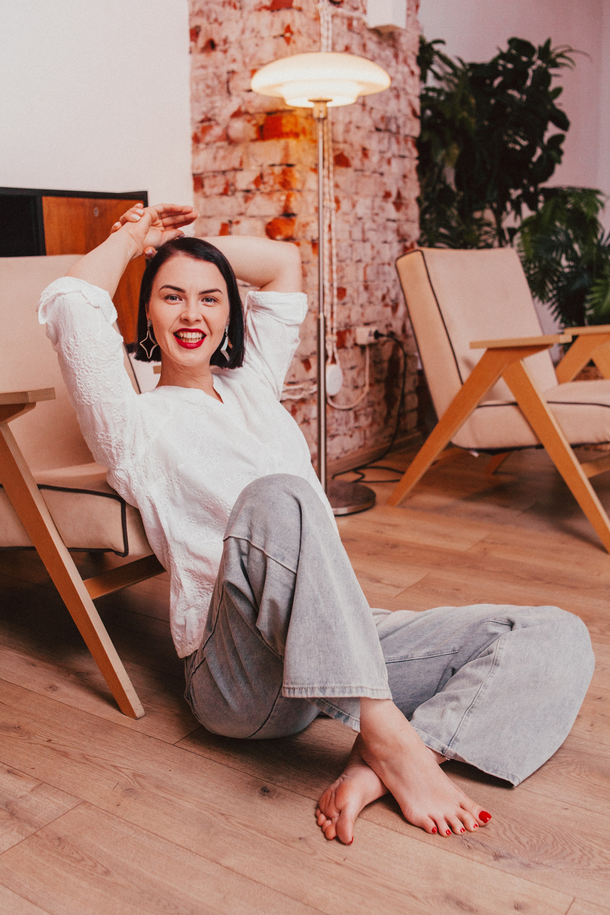 Женщина в кофте и джинсах позирует в хорошо обставленной комнате.