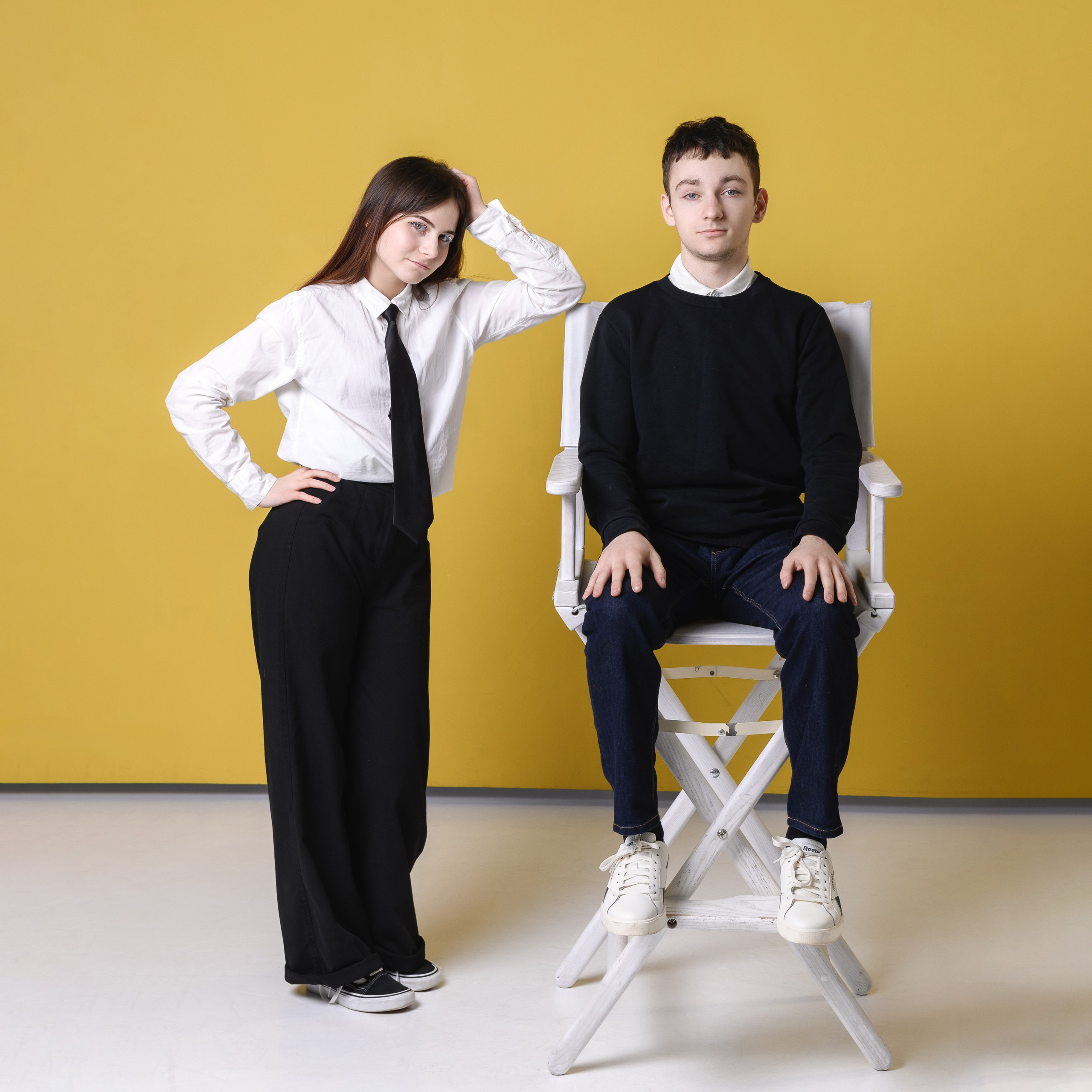 Студийный парный портрет на жёлтом фоне: девушка стоит рядом, юноша сидит на высоком стуле.