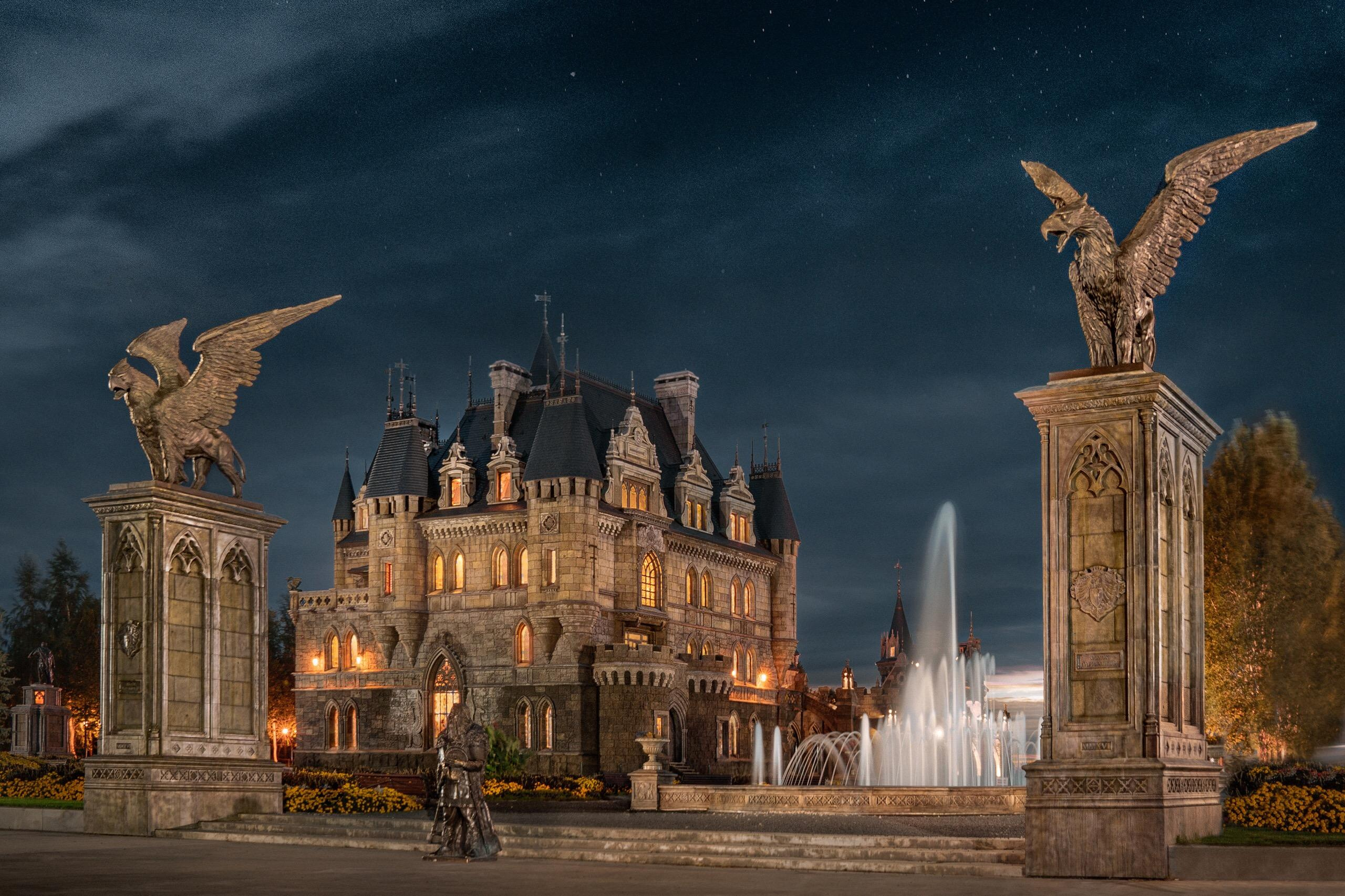 Ночной вид замка Гарибальди с подсветкой и фонтаном, окружённым крылатыми статуями грифонов, создающими величественную и сказочную атмосферу.