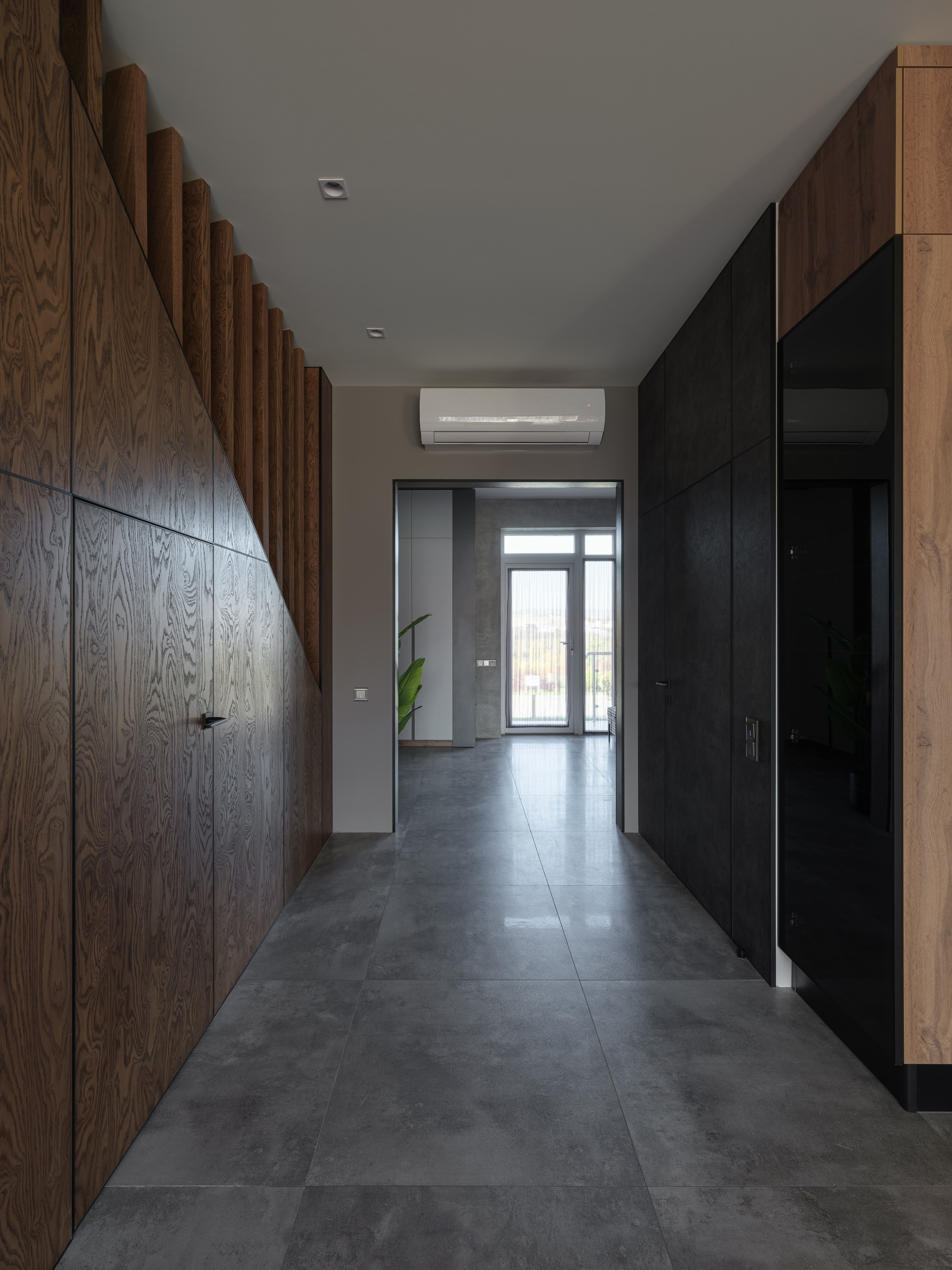 Современный коридор с большими серыми плитами на полу, деревянными панелями и встроенными шкафами. Лаконичный интерьер по проекту дизайнера Алины Дёровой, стилист Наталья Якушева, фотограф Сергей Денисенко.