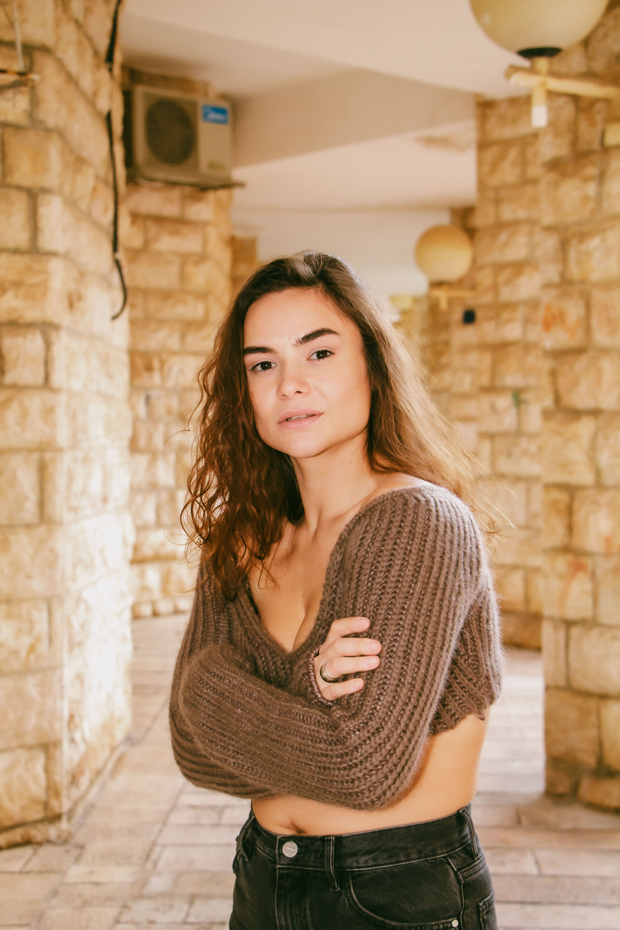 девушка возле каменного дома сложив руки смотрит в камеру