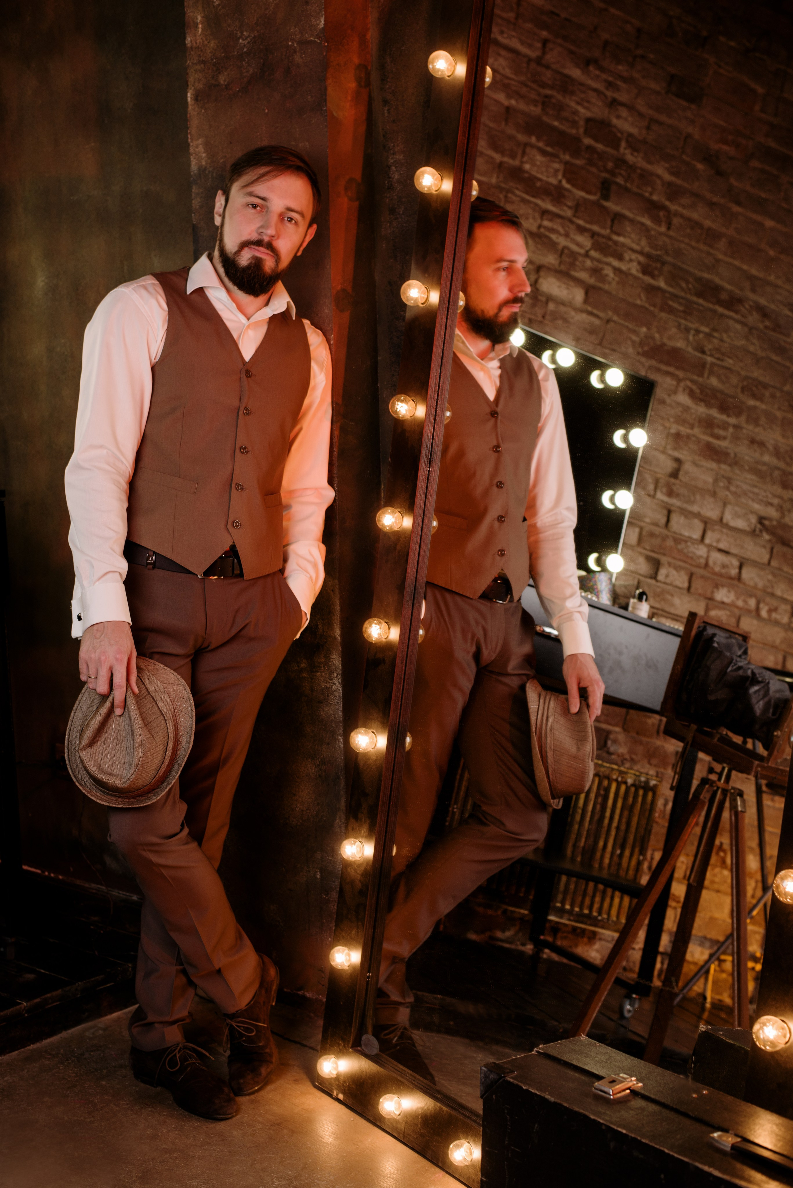 Мужчина в стиле ретро и жилете и белой рубашке держит в руках кепку на фоне ярких огней