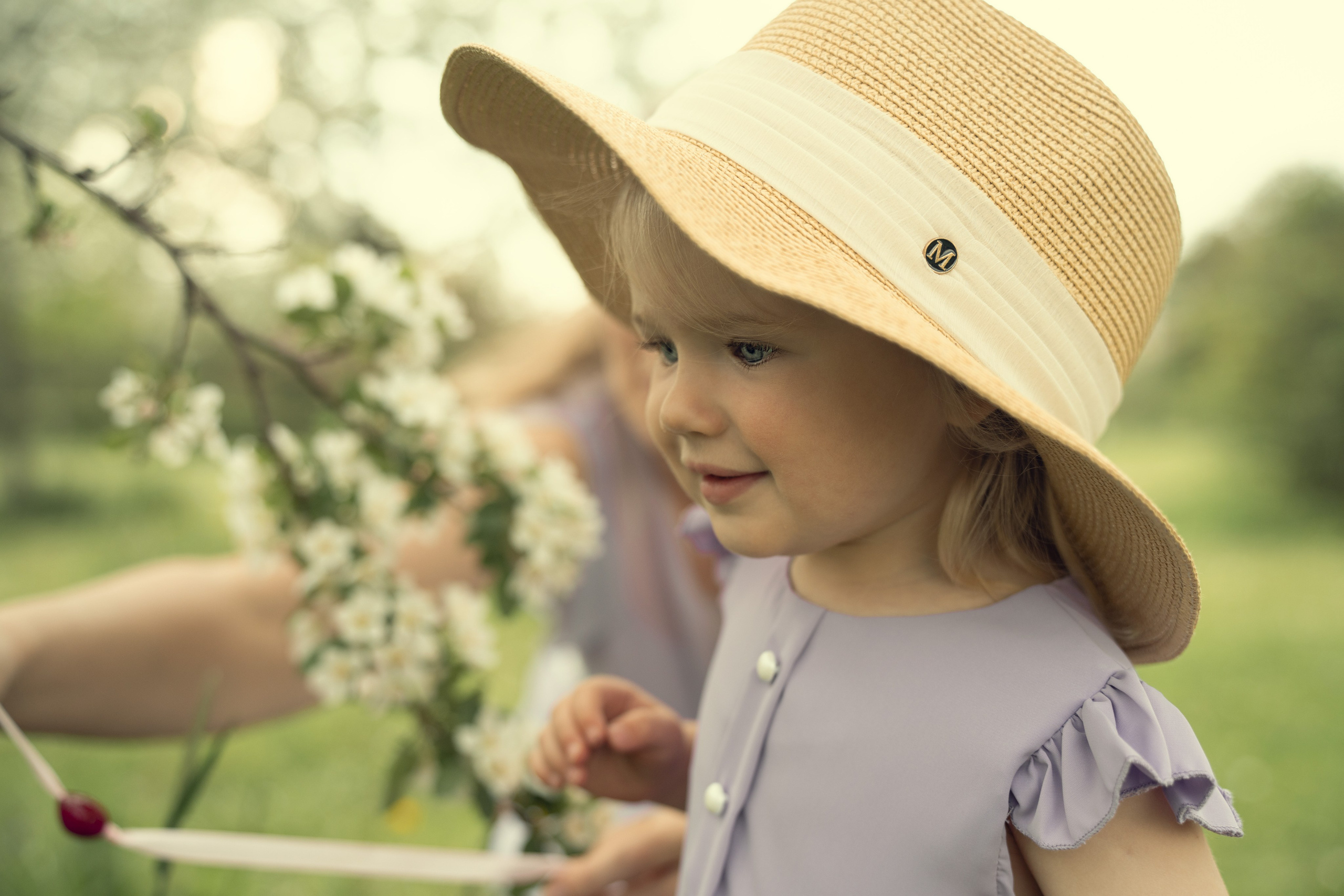 Портрет ребенка в шляпе в цветущем яблоневом саду летом.