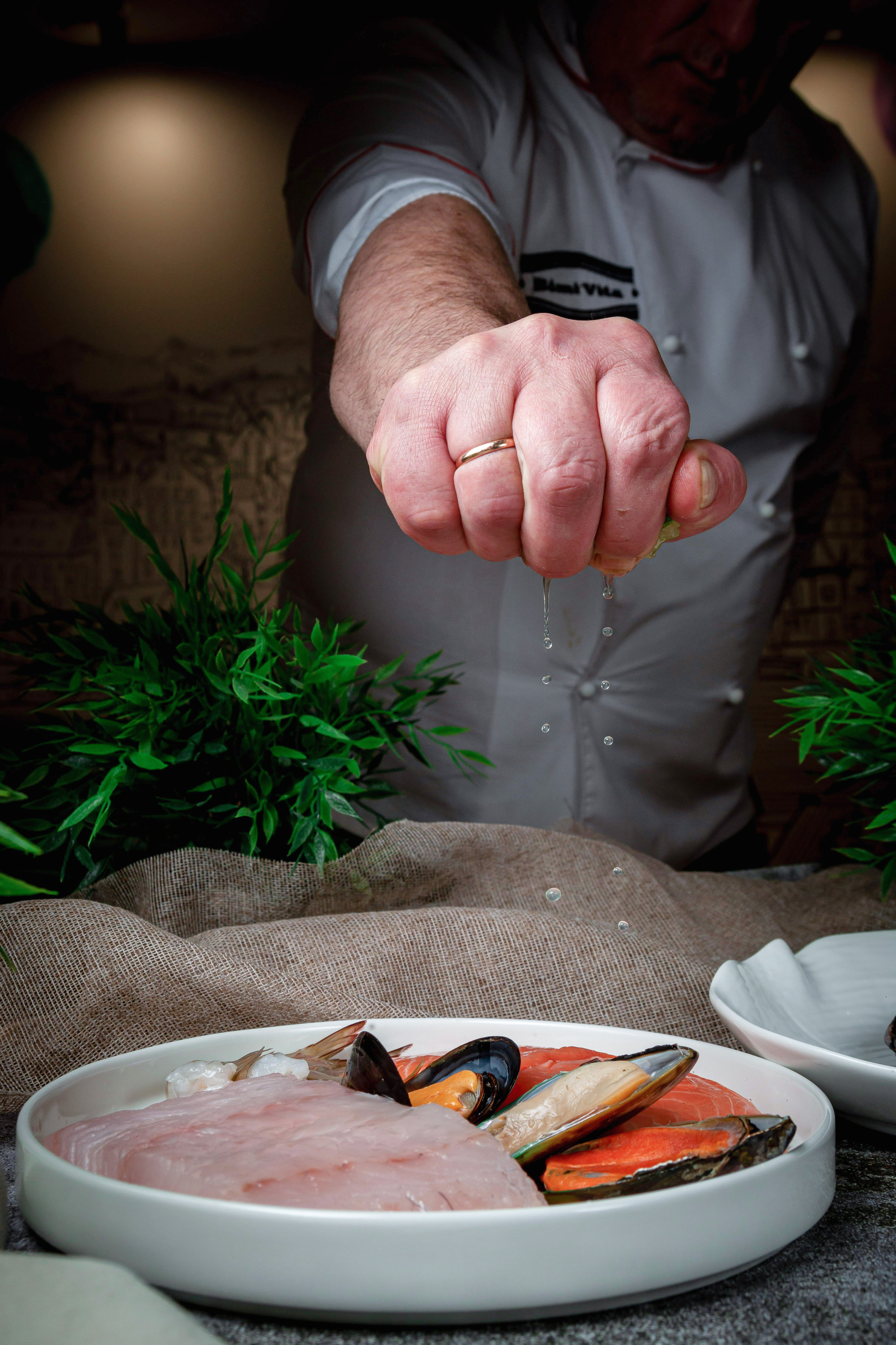 Шеф повар в ресторане поливает блюдо лимонным соком