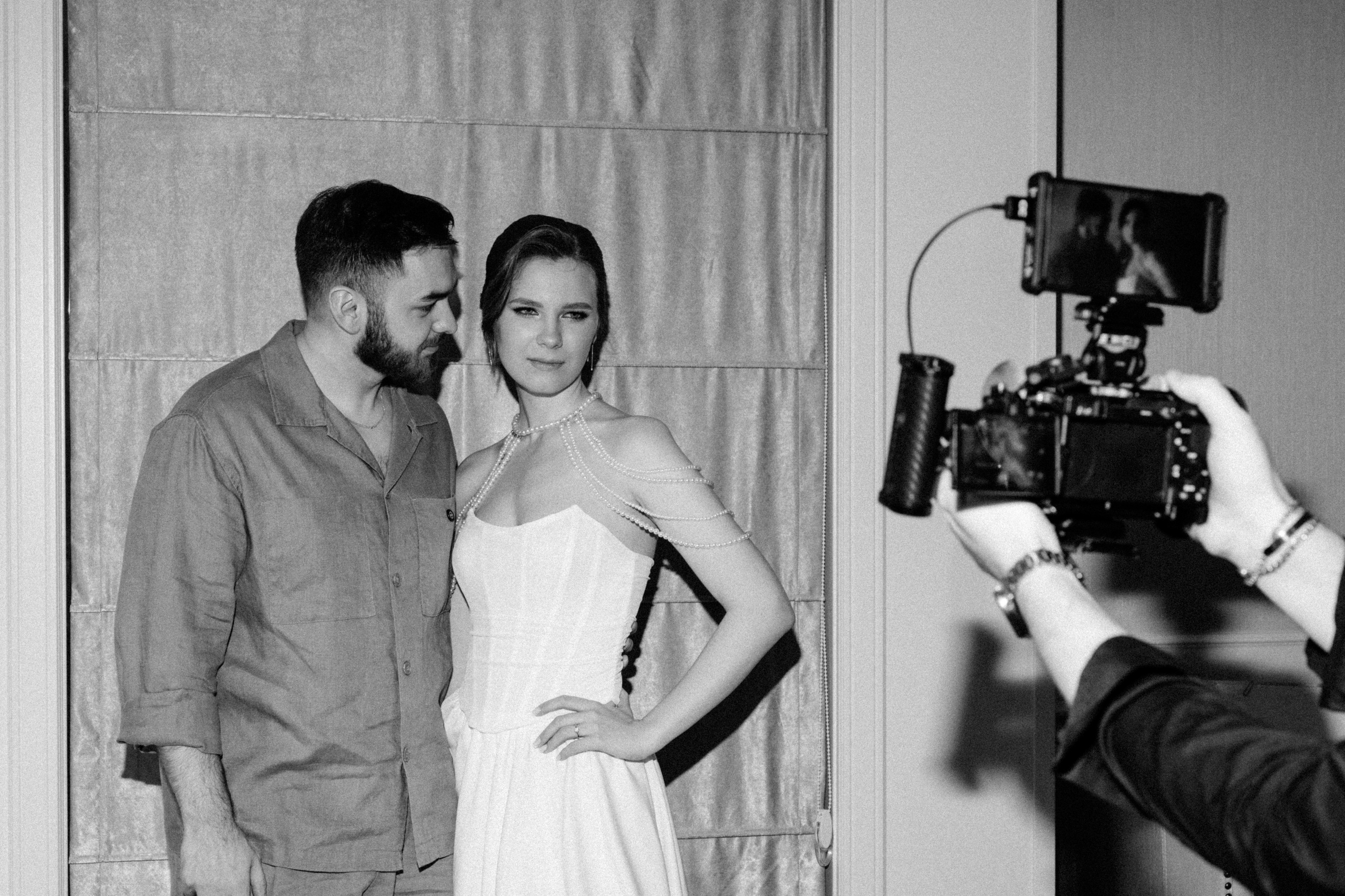 Черно-белое фото жениха и невесты, позирующих рядом с кинокамерой.