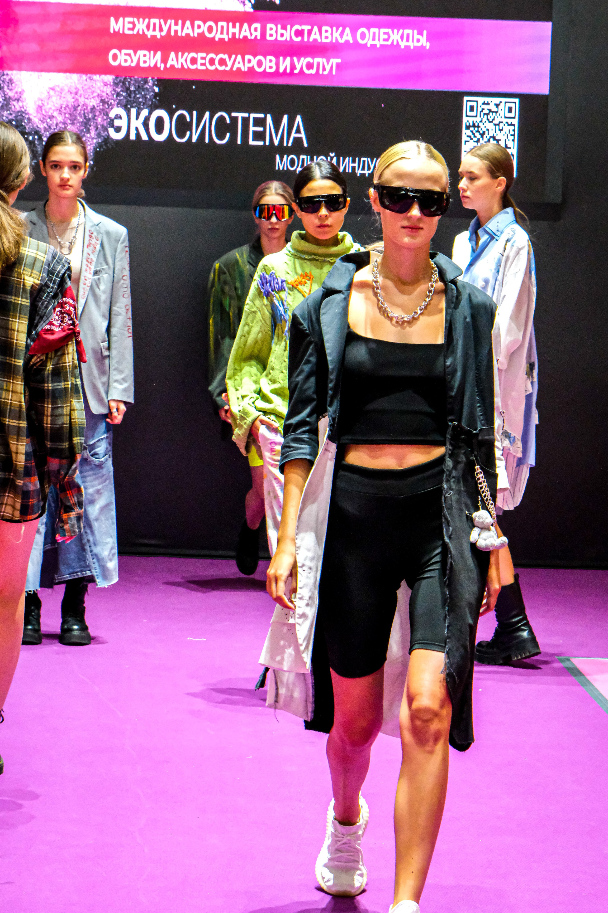  "Модели в ярких нарядах проходят по подиуму во время показа мод, освещенные яркими софитами и окруженные восторженными зрителями."