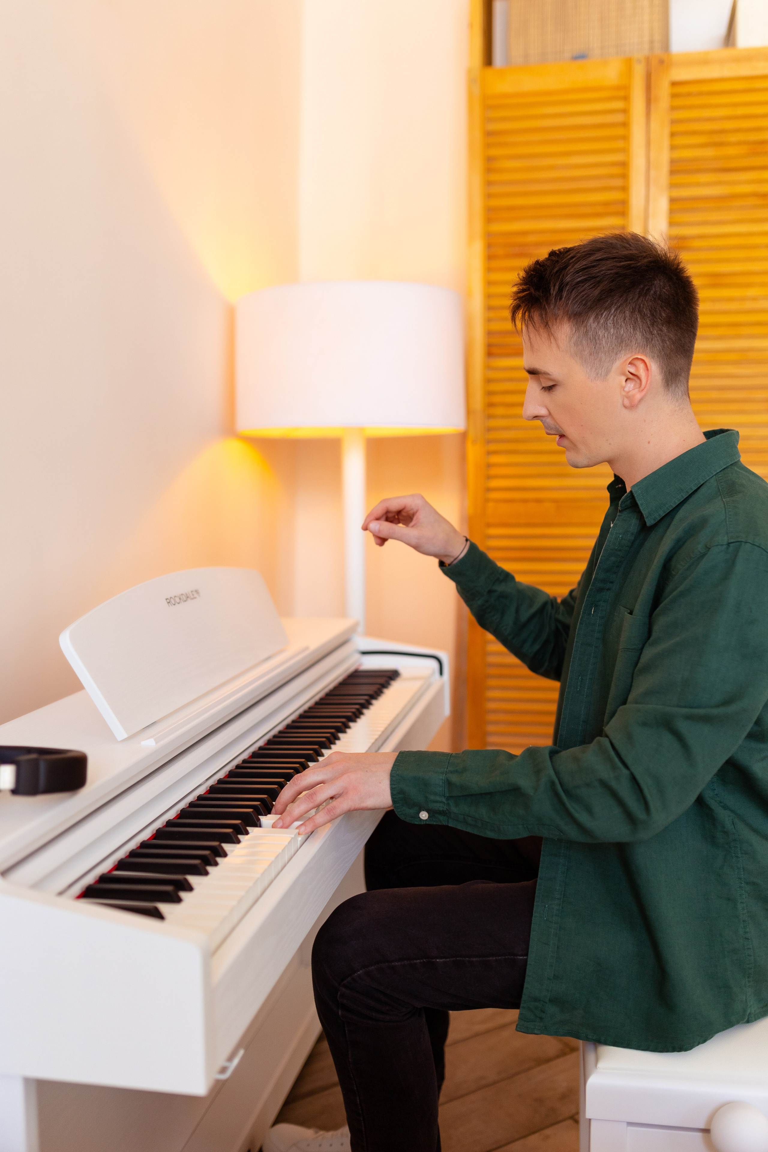 На фоне светящегося торшера юноша играет на белом пианино