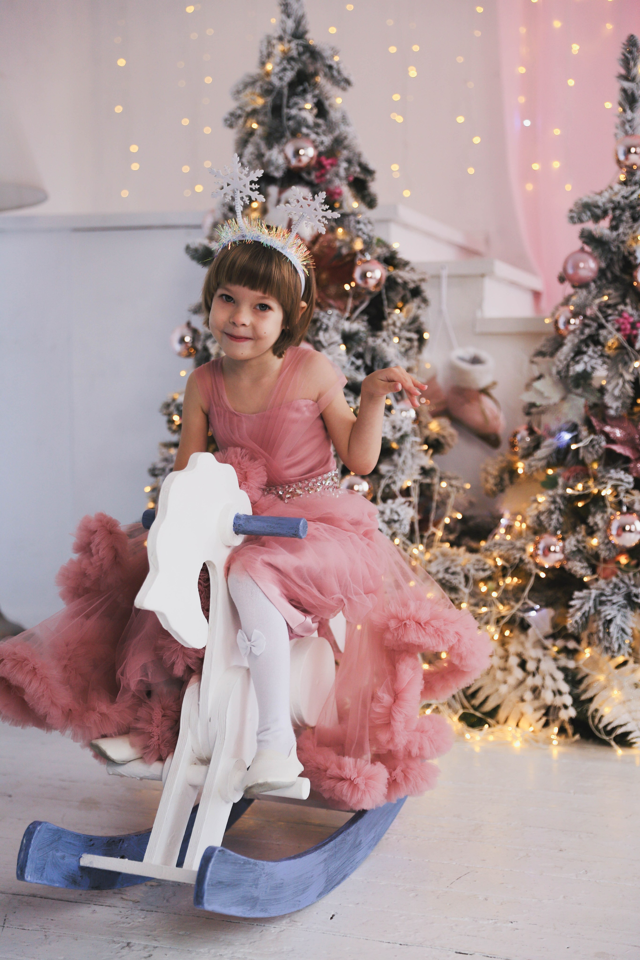 Радостная девочка на новогодней фотосессии верхом на деревянном качалке коне
