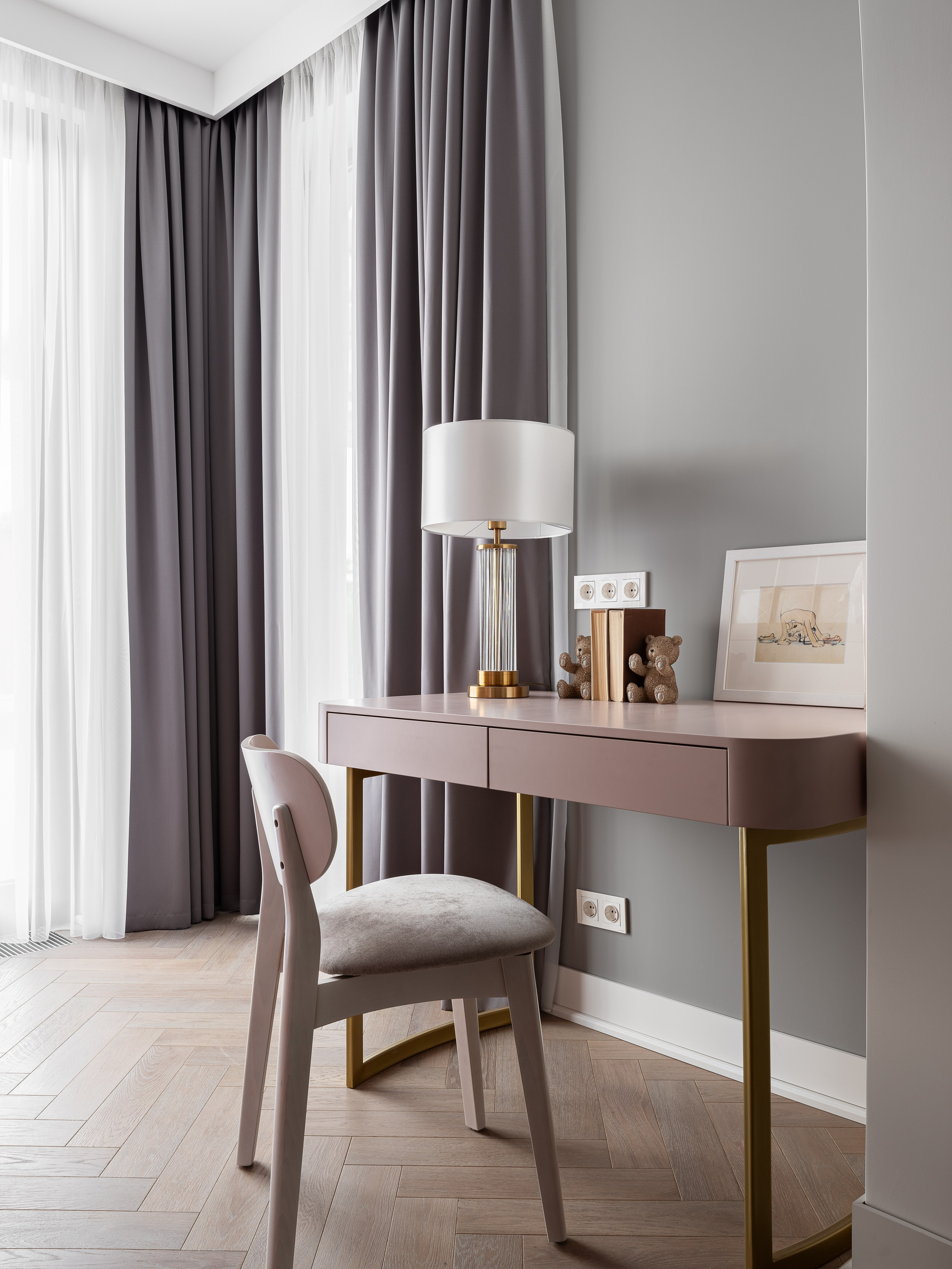 Уютное рабочее место в детской с розовым письменным столом, серым креслом, стильной настольной лампой и серыми шторами на окне, выполненное дизайнером Василиссой Бачевой, стилистом Натальей Якушевой и запечатленное фотографом Сергеем Денисенко.