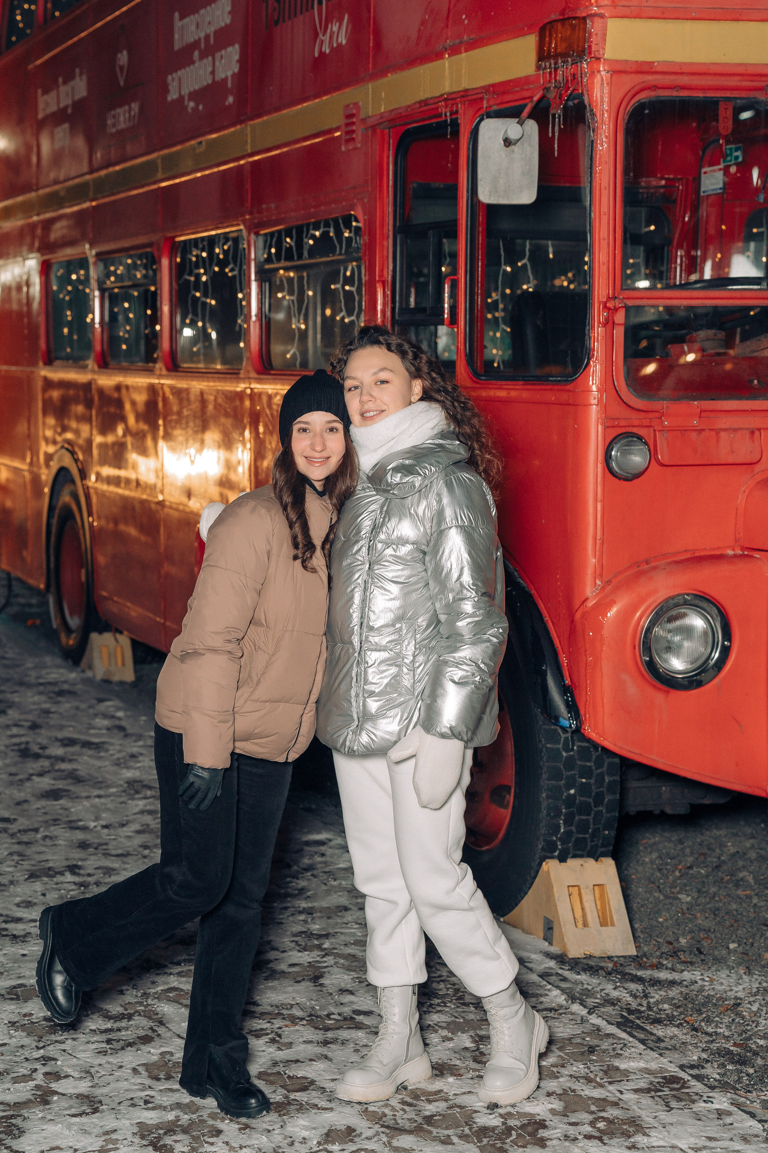 Две двушки позируют у красного автобуса.