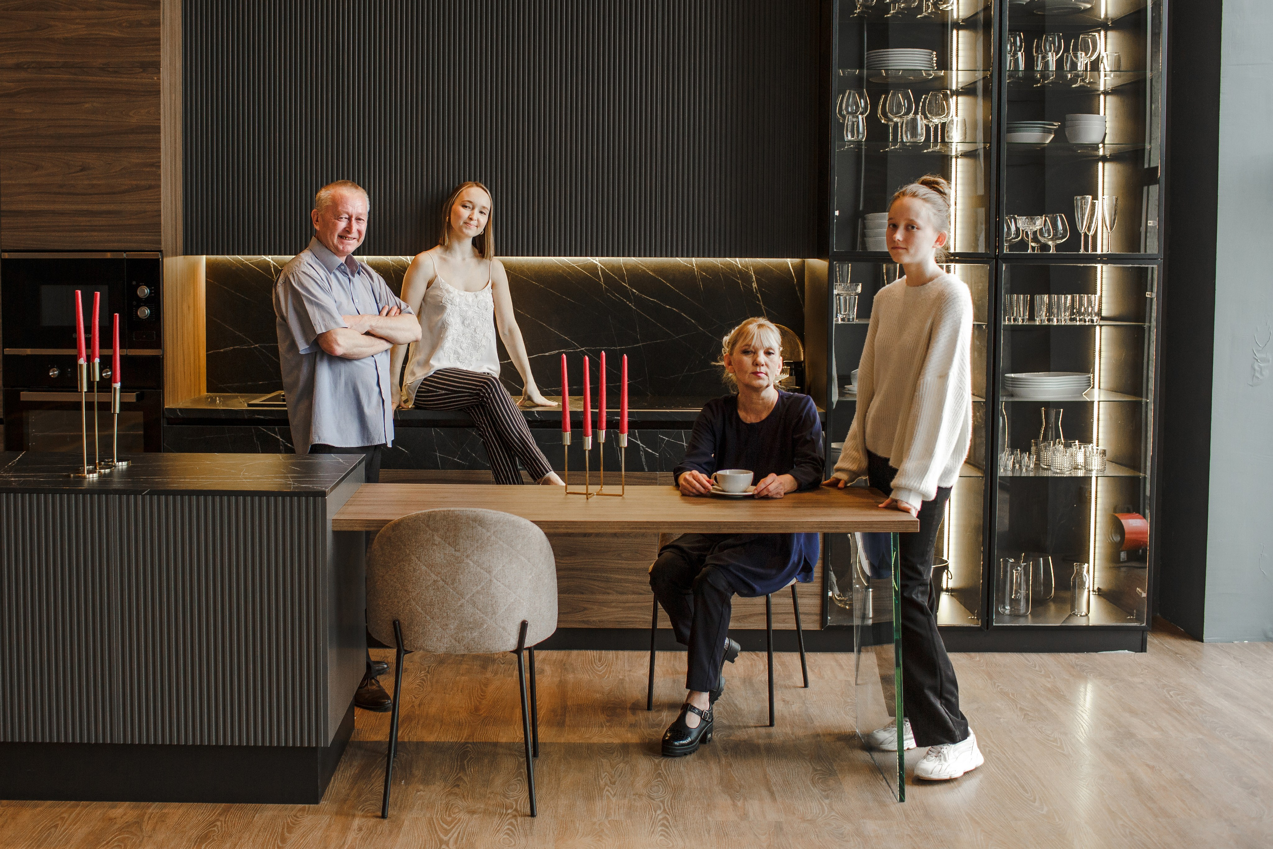 Семейный портрет на стильной кухне в темных тонах: за столом собралась семья из четырех человек.