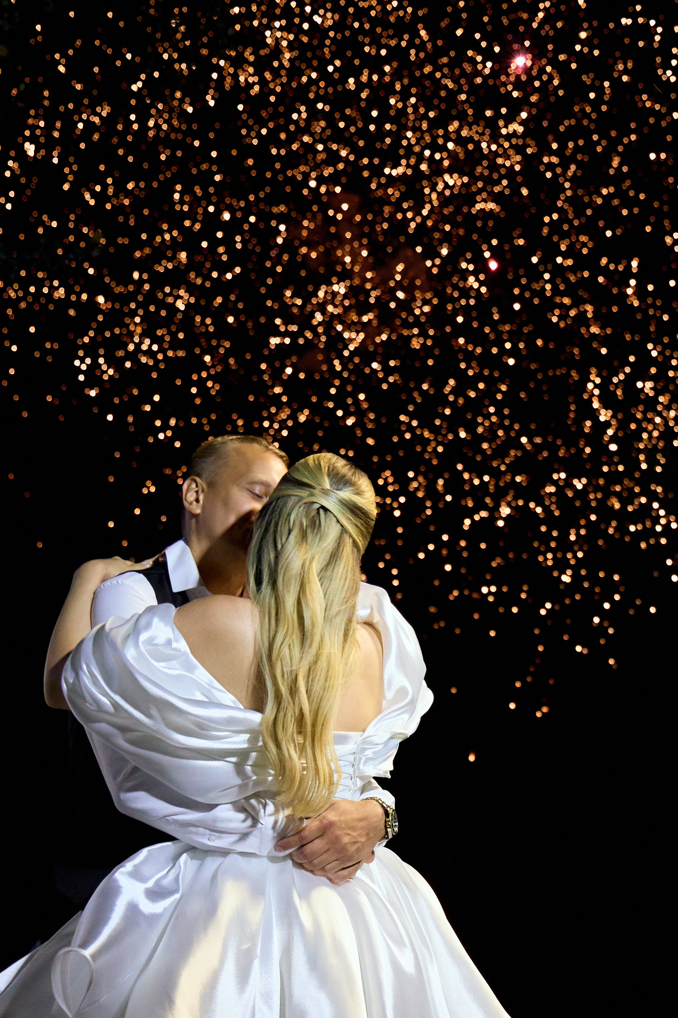 Фотосессия молодых на фоне салюта. Нежные объятия невесты и жениха.