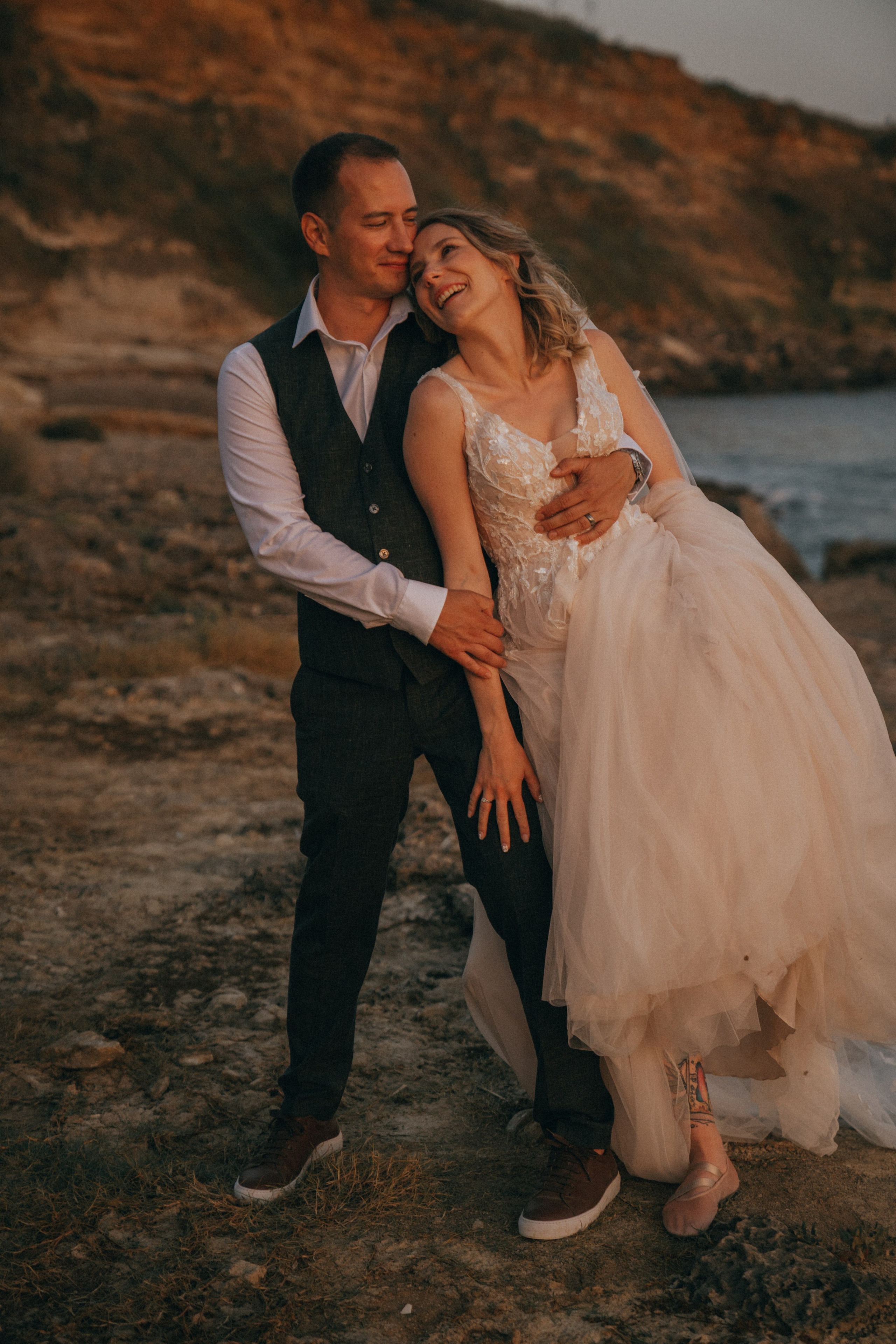 Счастливая пара жених и невеста целуется на фоне волн  скал и заката у моря океана.