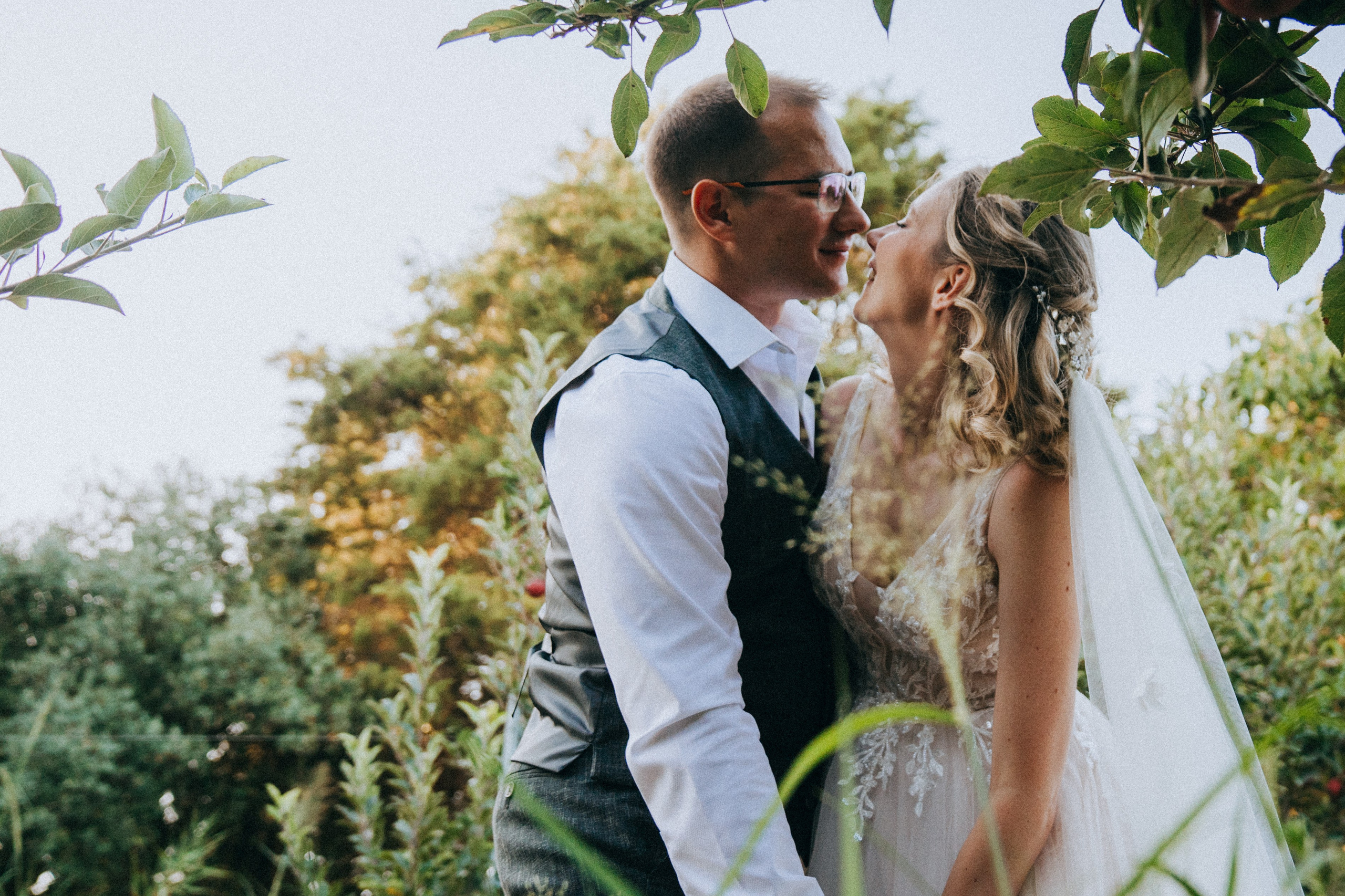 Жених и невеста обнимаются среди яблоневого сада, вокруг созревшие яблоки.