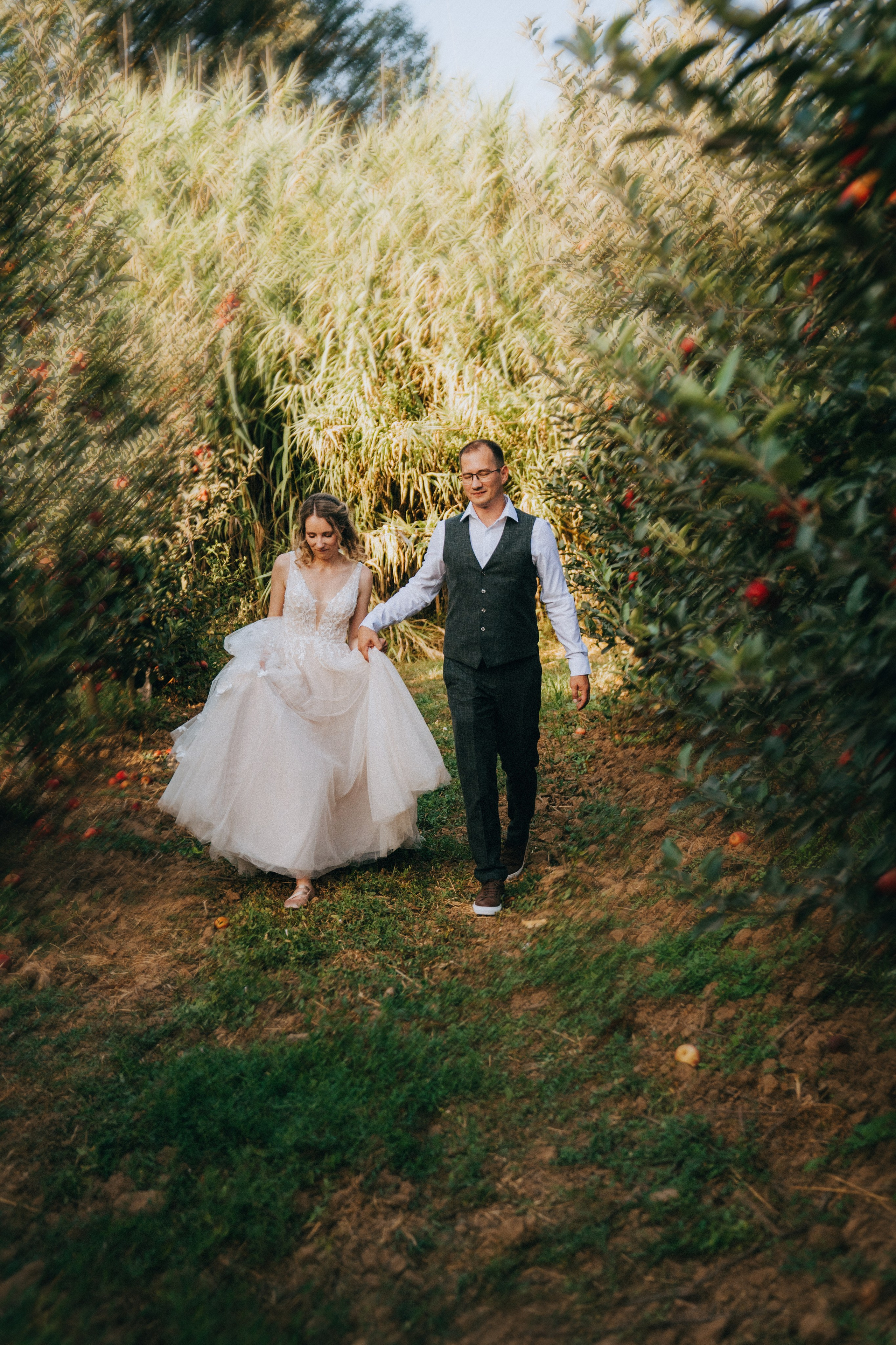 Жених и невеста бегут среди яблоневого сада, вокруг созревшие яблоки.