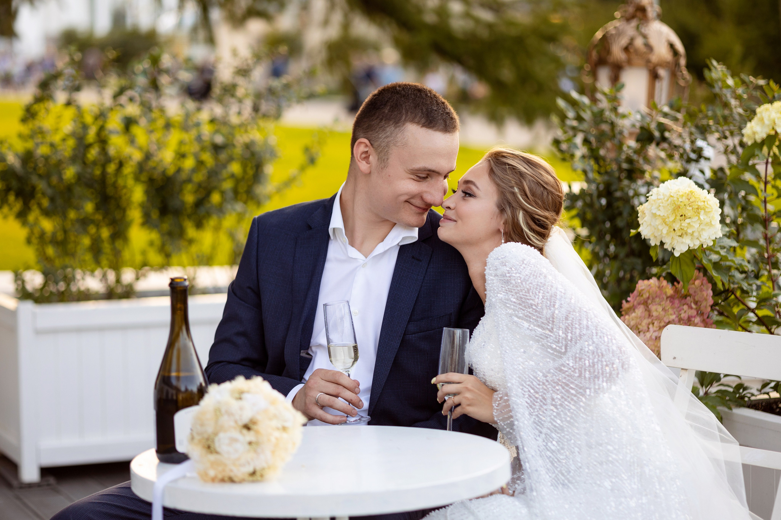 Молодые сидят за круглым столом на фоне розового куста.