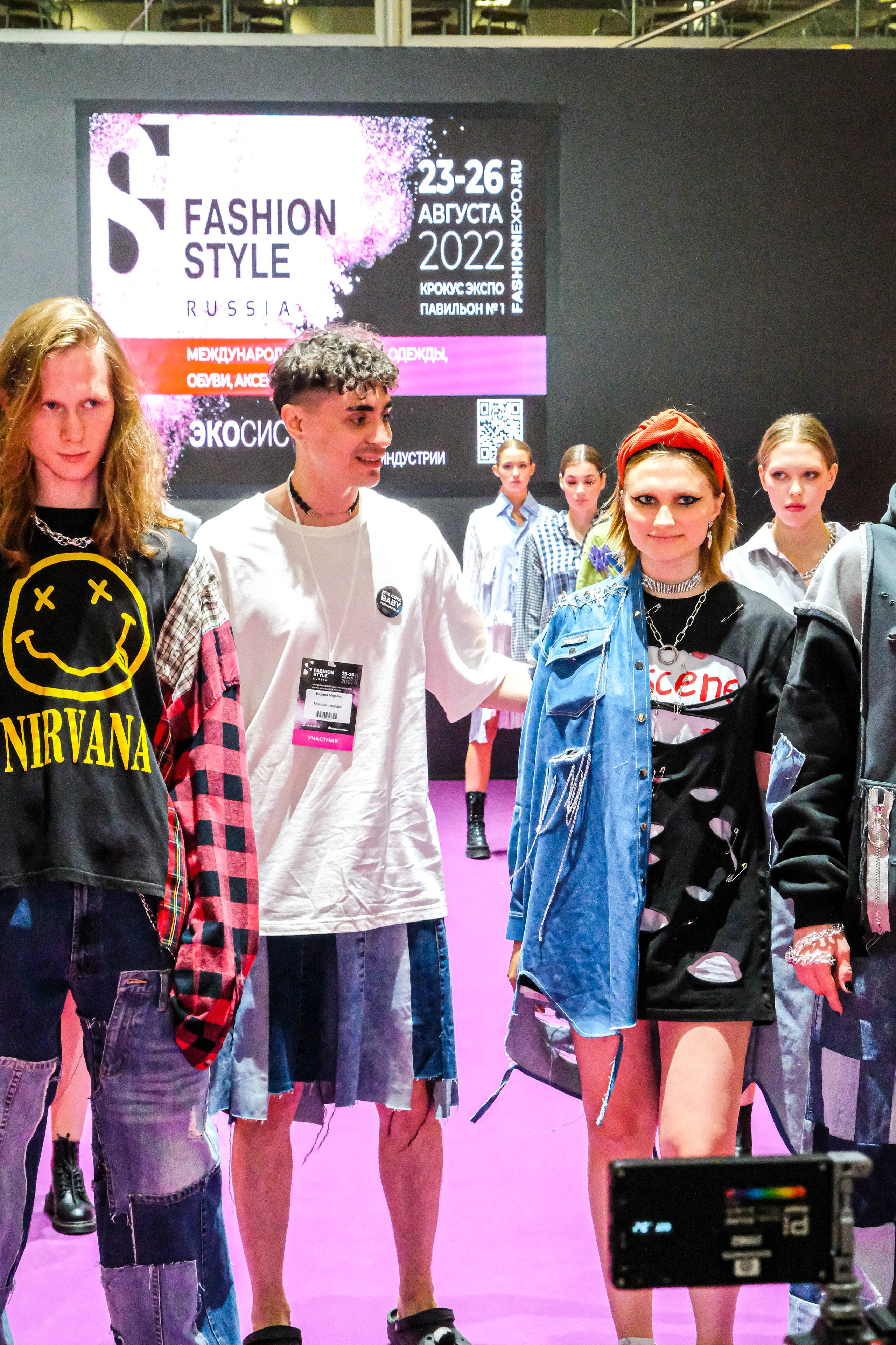  "Модели в ярких нарядах проходят по подиуму во время показа мод, освещенные яркими софитами и окруженные восторженными зрителями."