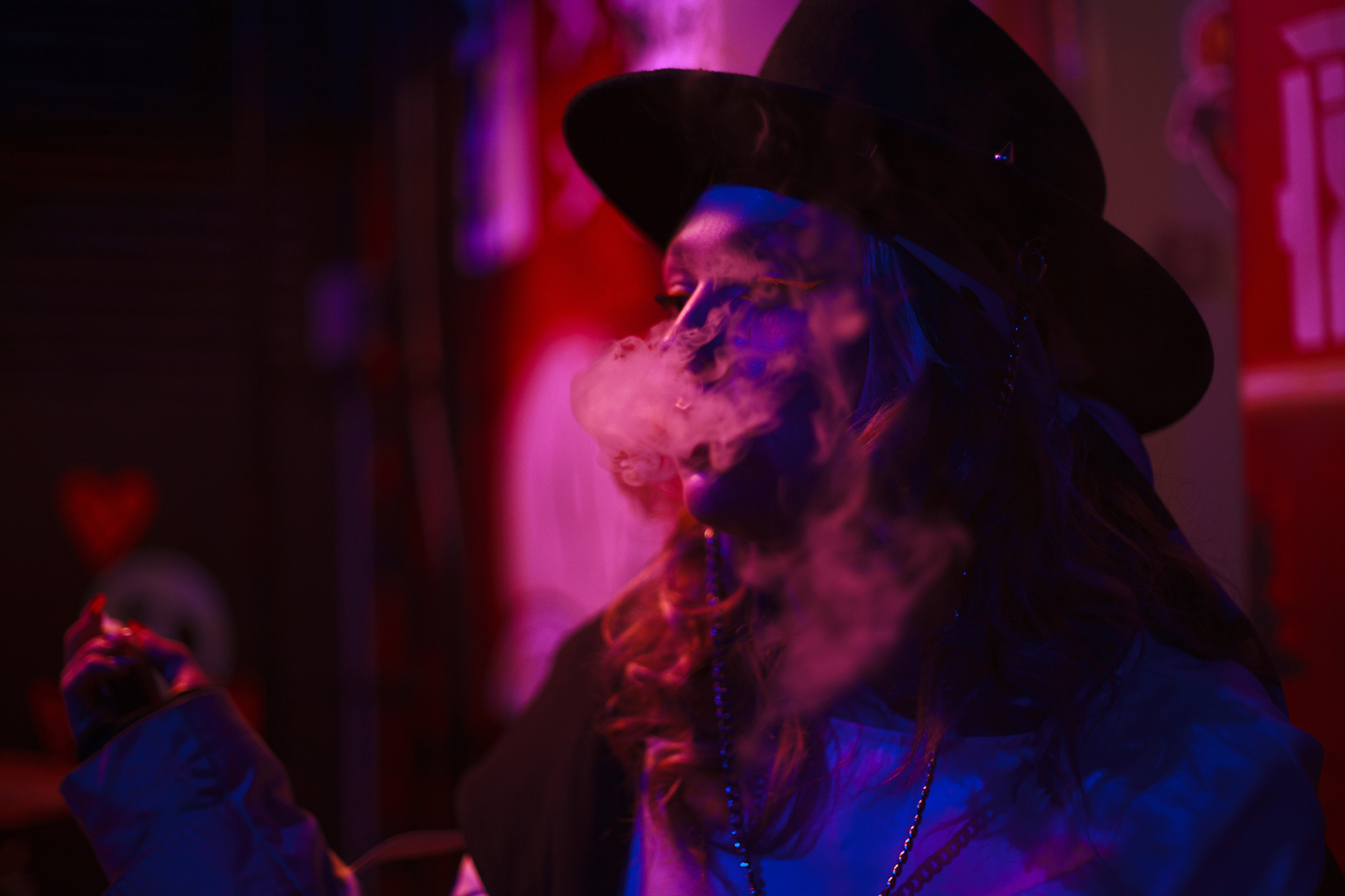 Девушка в шляпе пускает дым в неоновых огнях