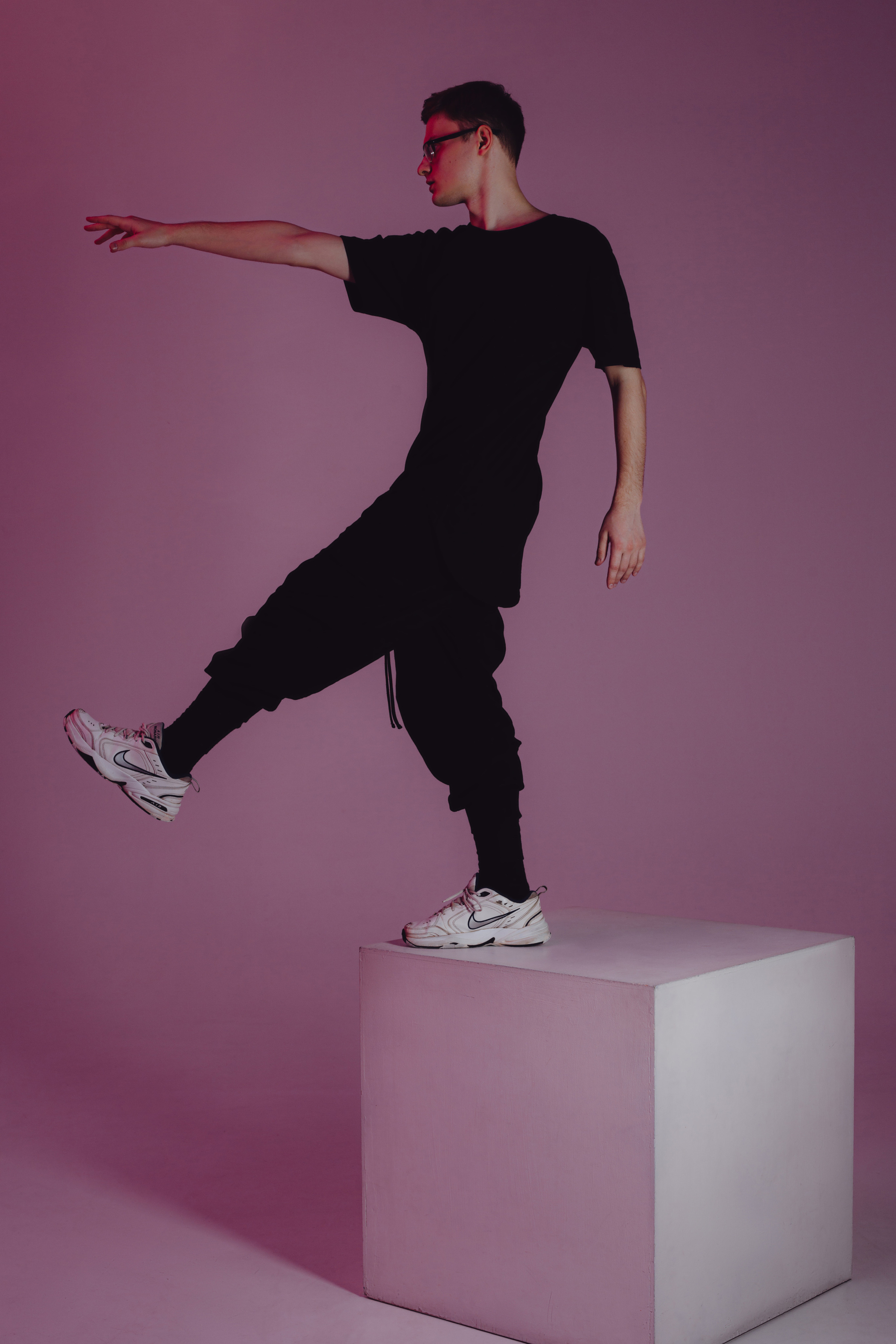 Парень стоит на белом кубе на розовом фоне