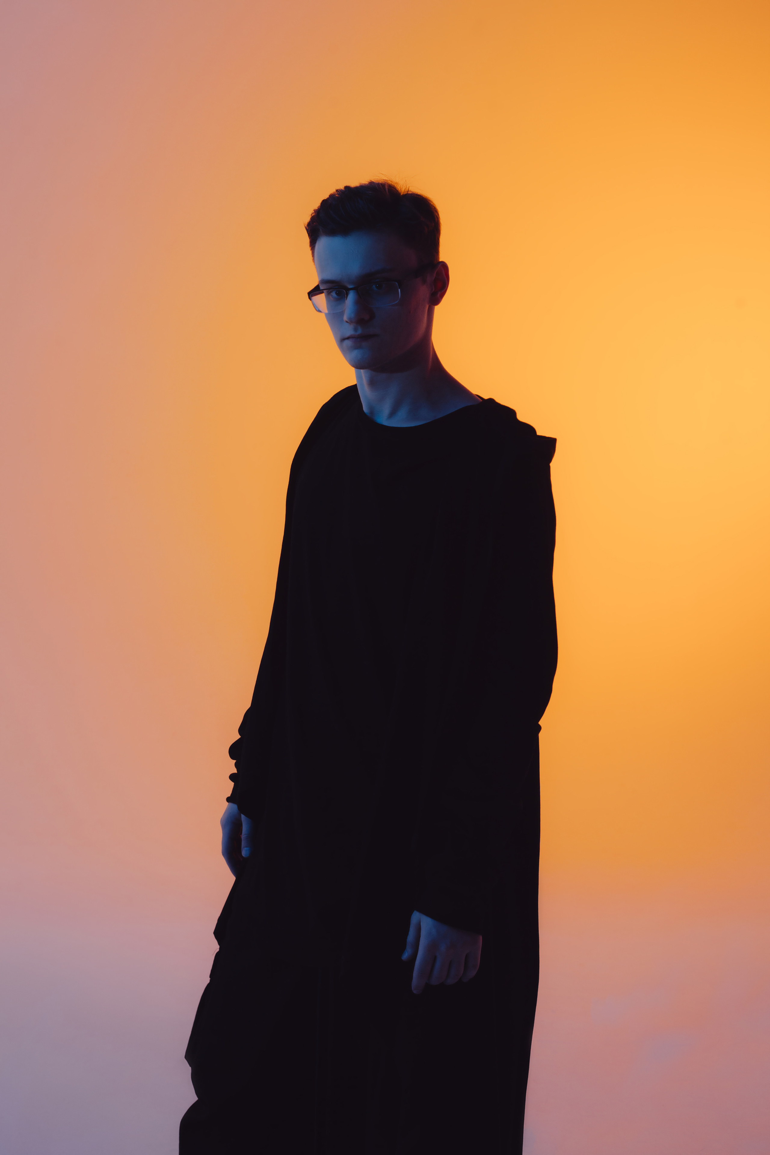 Молодой человек в черном балахоне на фоне желтого градиента