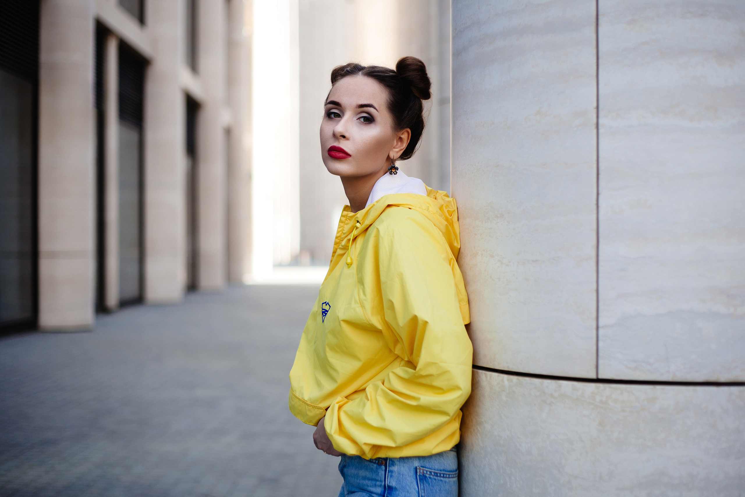 Девушка в желтом плаще с капюшоном и синих джинсах гуляет по городу среди колонн