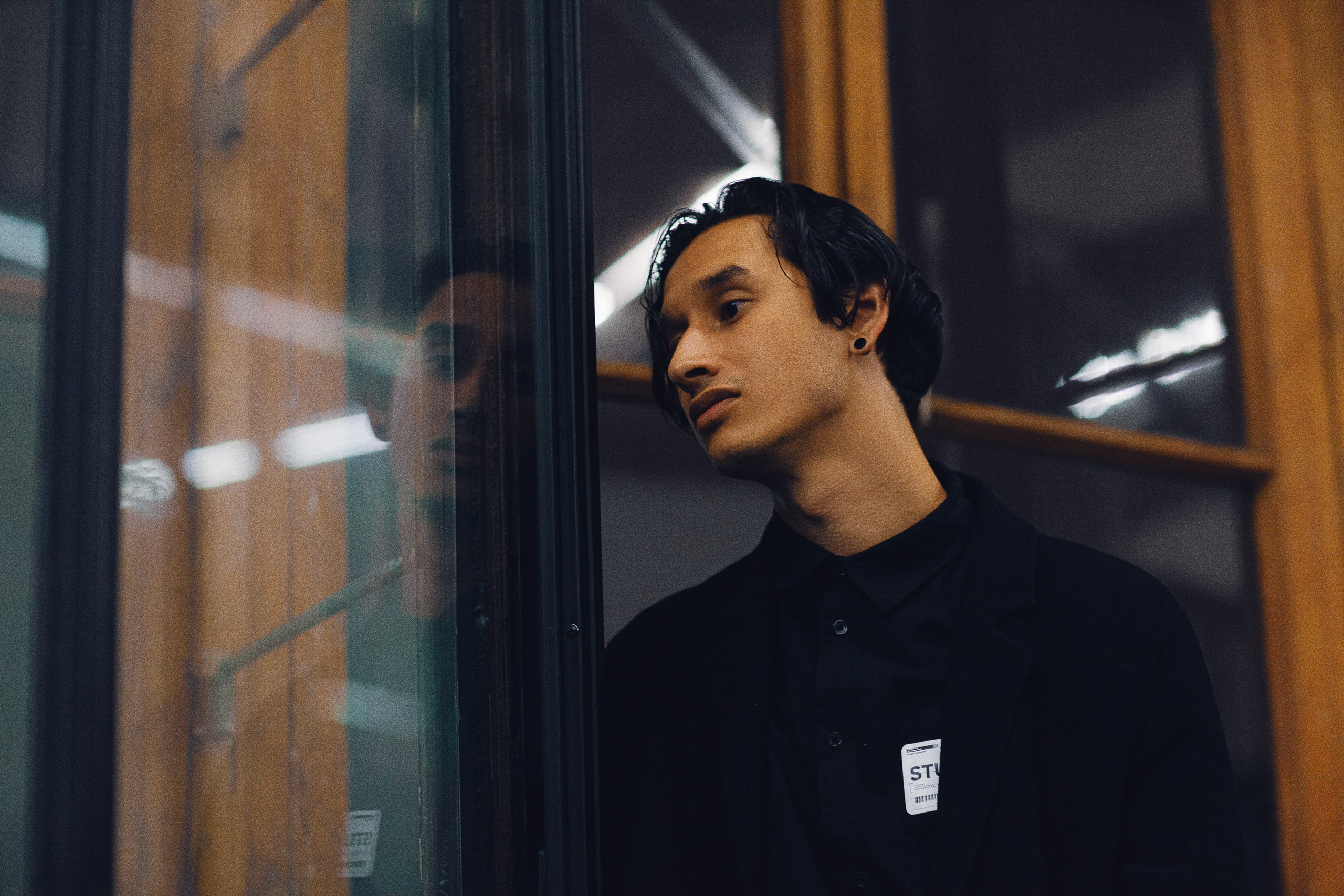 Молодой человек в черной одежде в помещении на фоне стекла отражений