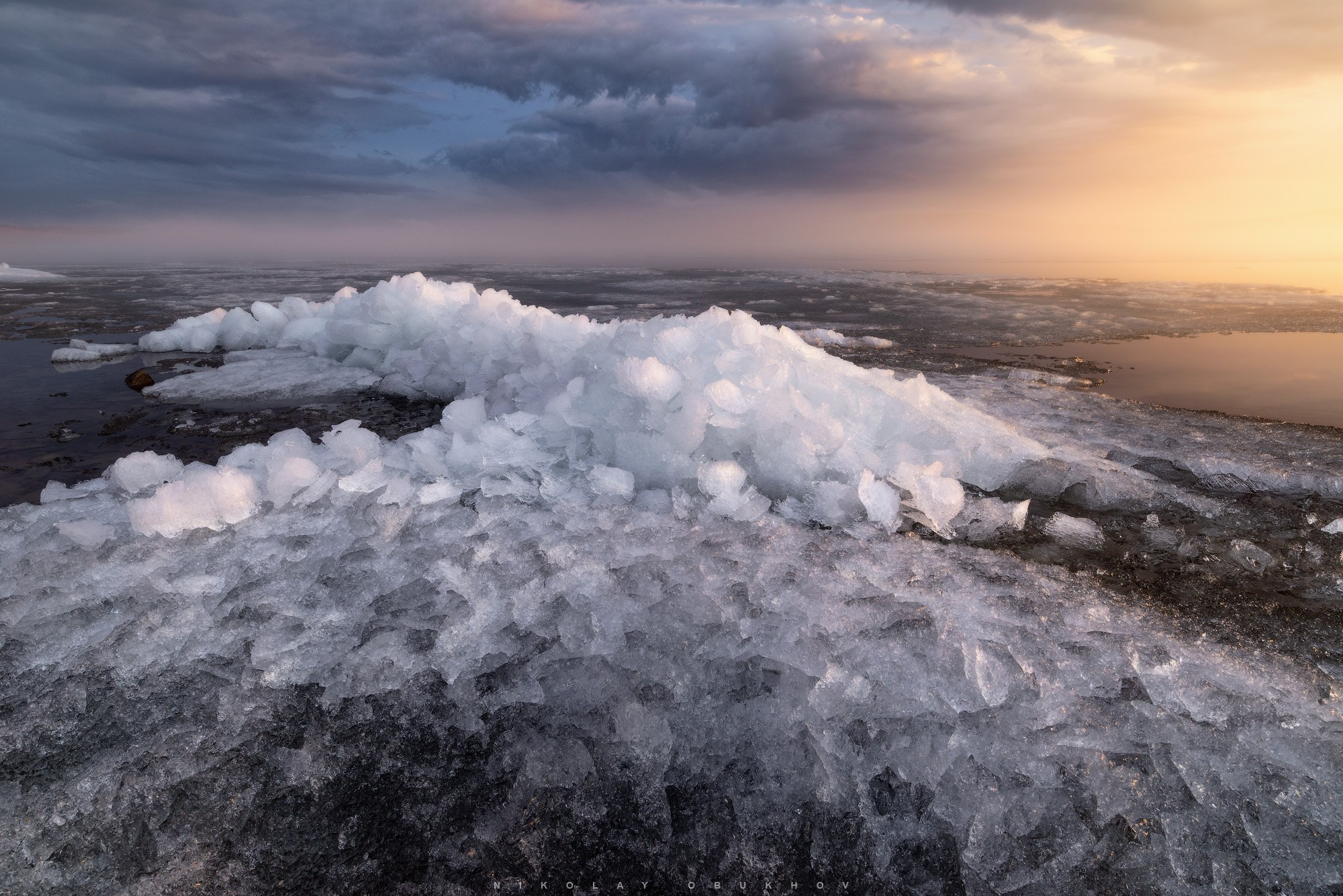 Красивый пейзаж в Свердловской области: закат окрашивает остатки льда на Черноисточинском пруду в золотистые тона, туман скрывает горизонт.