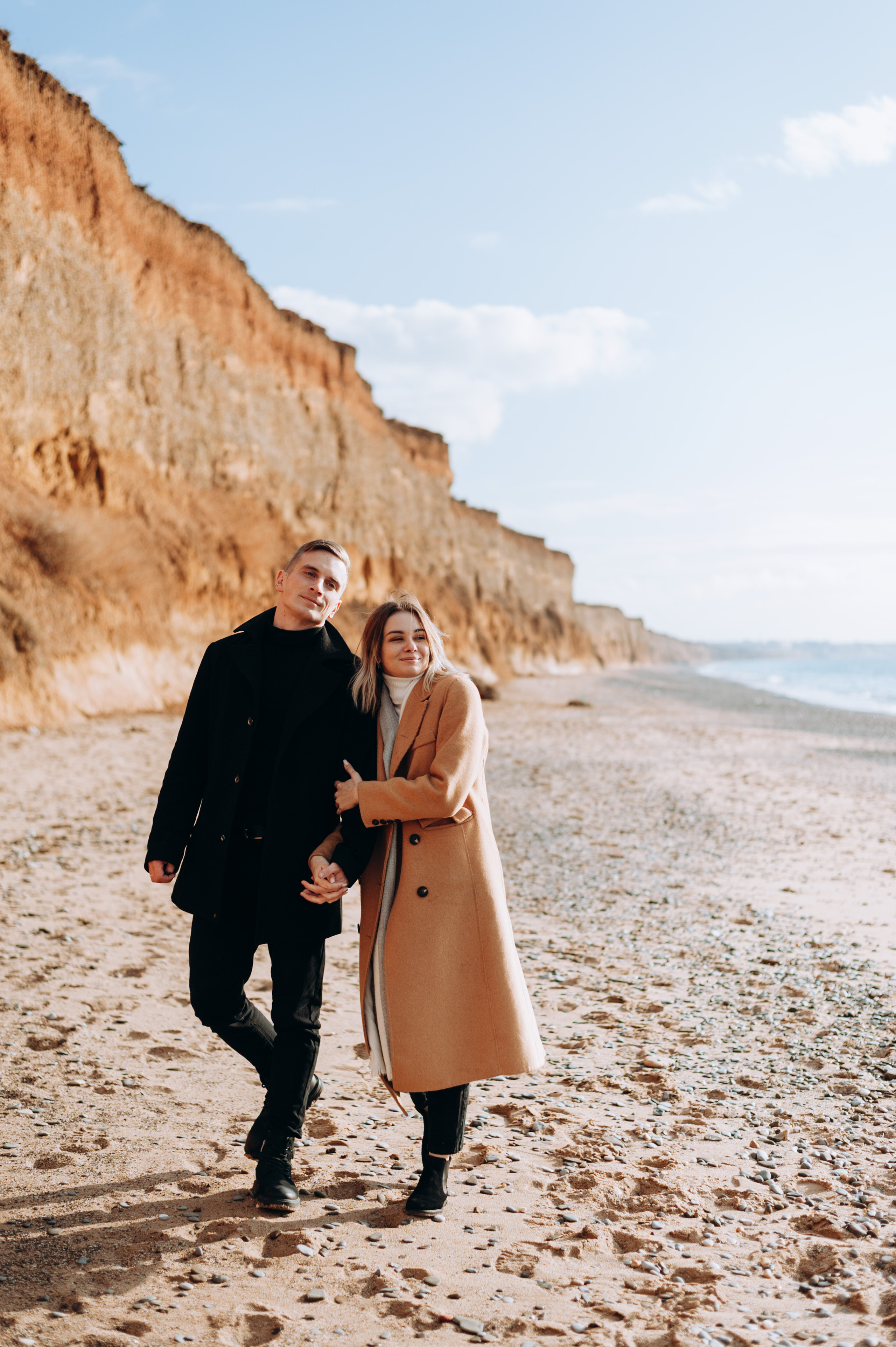 Парень и девушка в пальто гуляют по пляжу в Николаевке зимой у моря