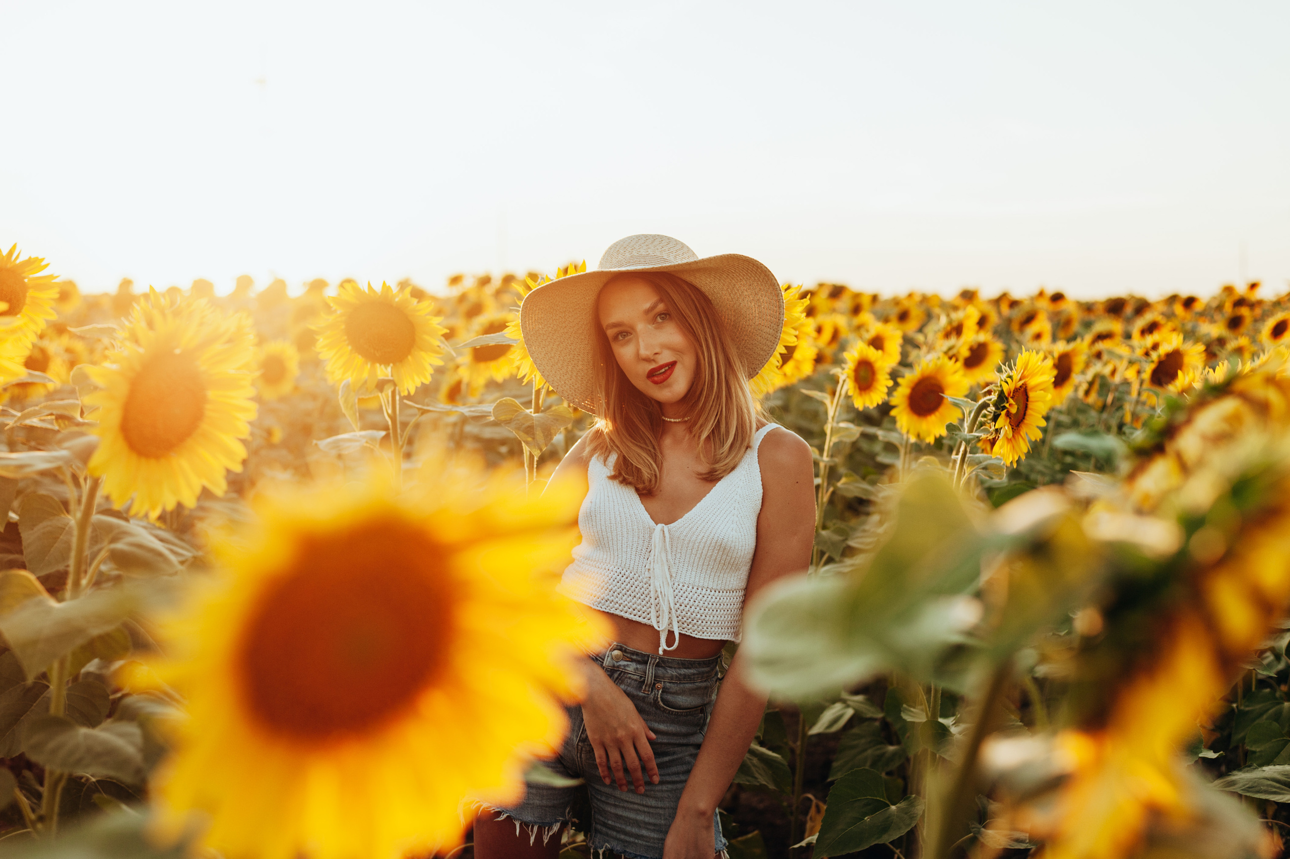 Девушка в соломенной шляпе среди подсолнухов на закате