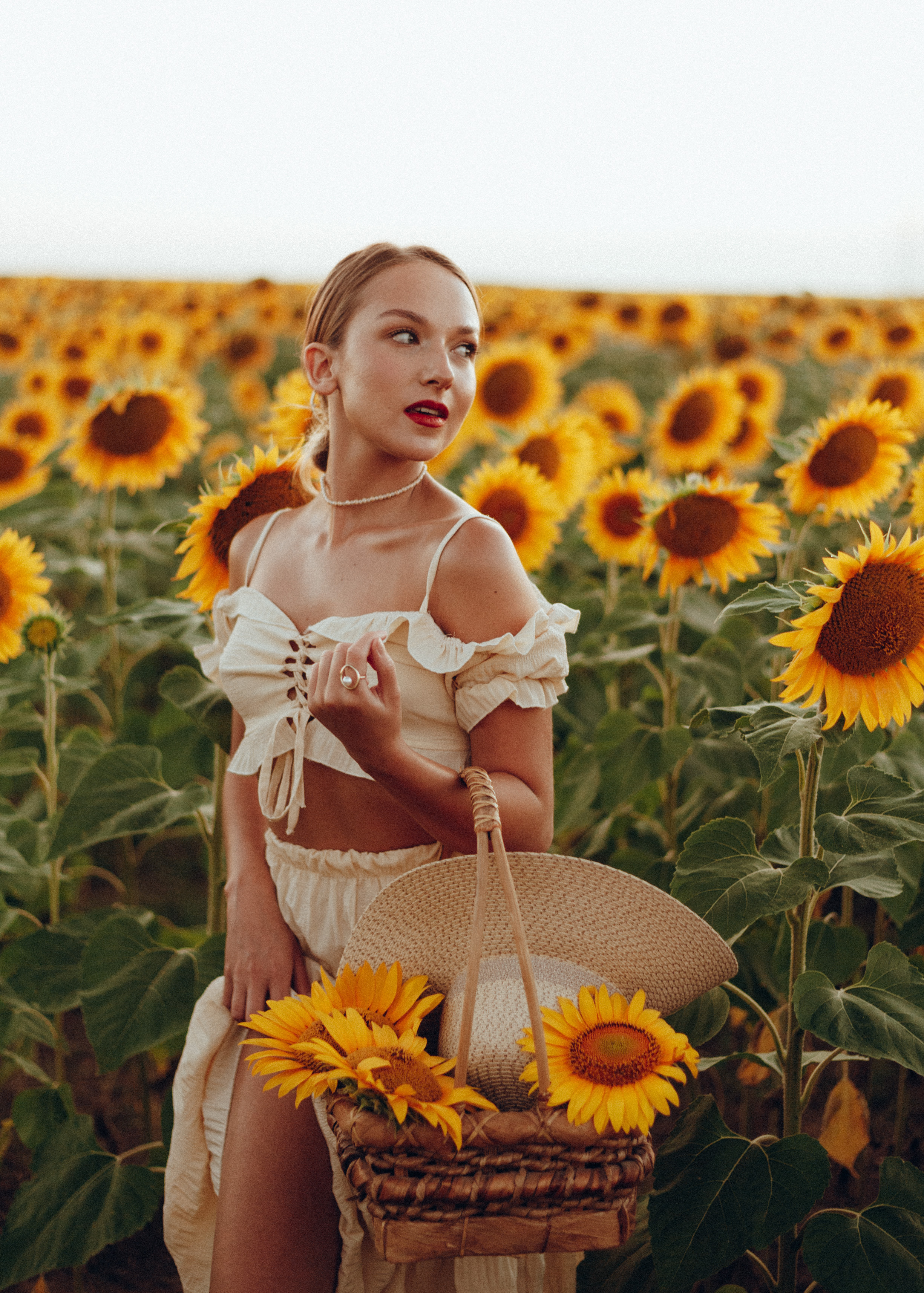 Девушка с плетеной корзиной в поле подсолнухов в летнем костюме