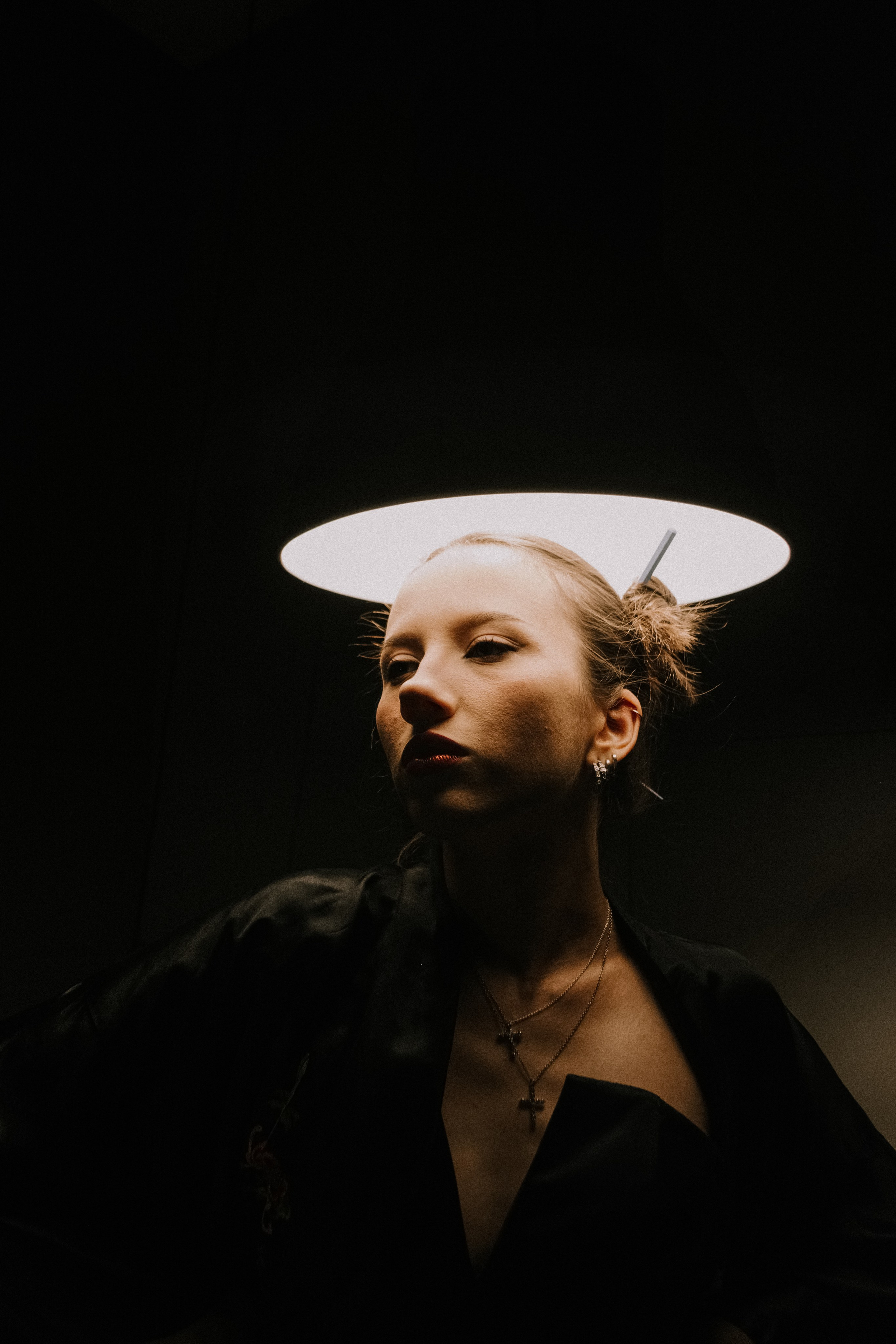 Крупный портрет девушки, освещаемой сверху большой лампой и стоящей прямо под ней 