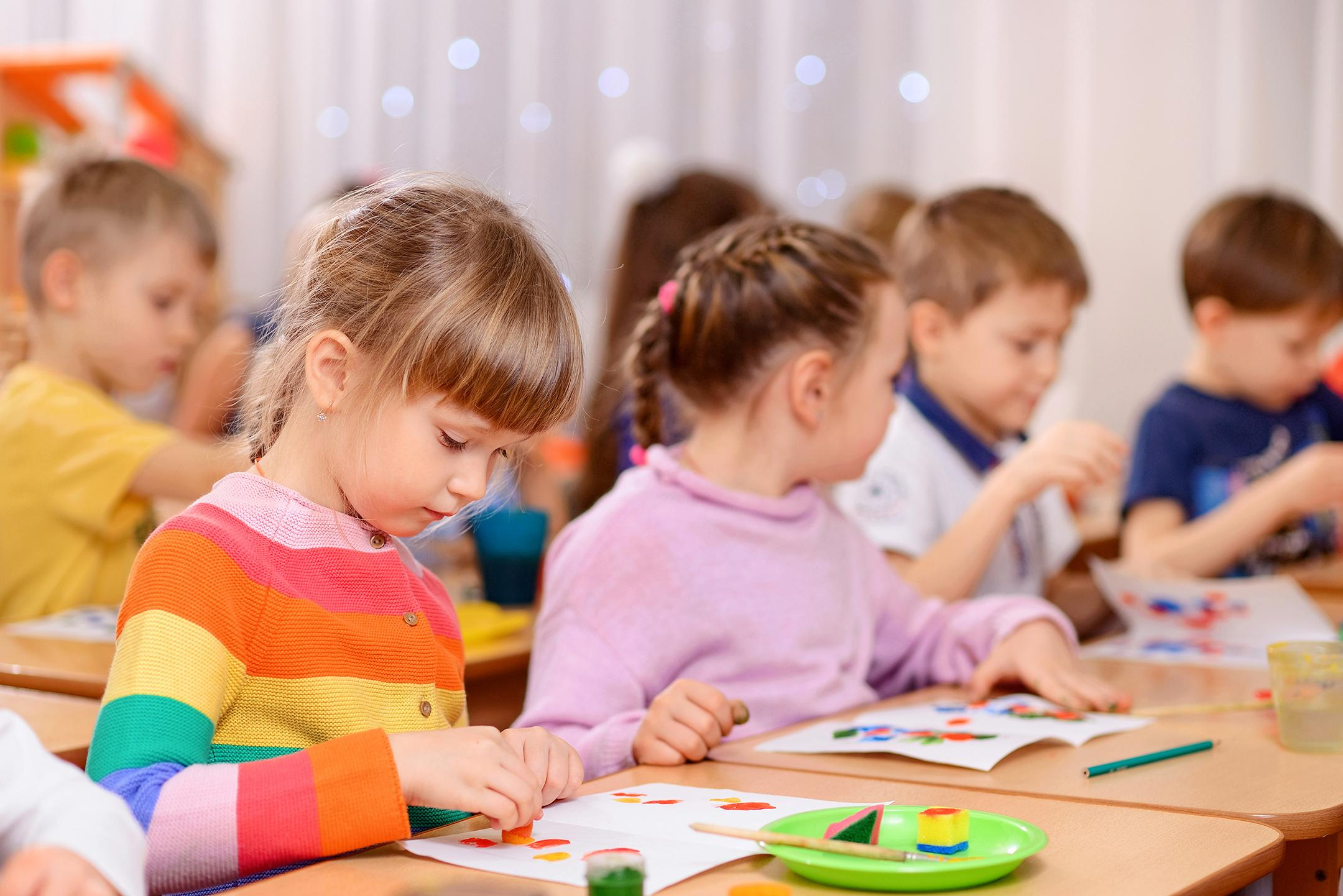 Дети в детском саду сидят за партами на занятии по рисованию