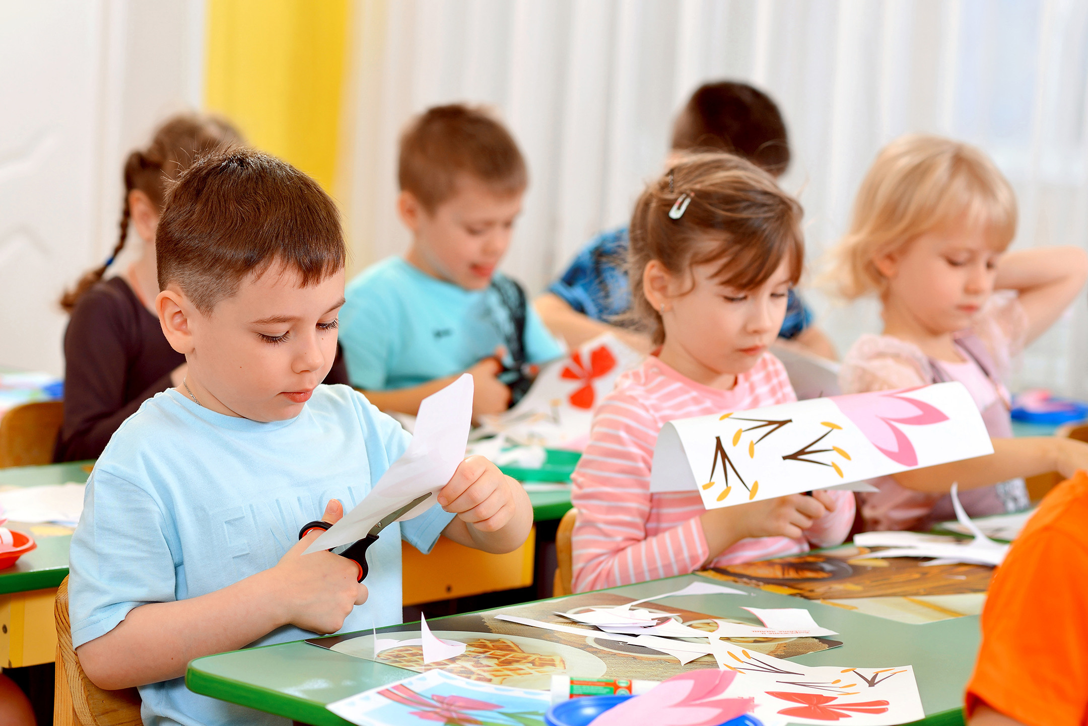 Дети за партами на занятии в детском саду вырезают ножницами цветы