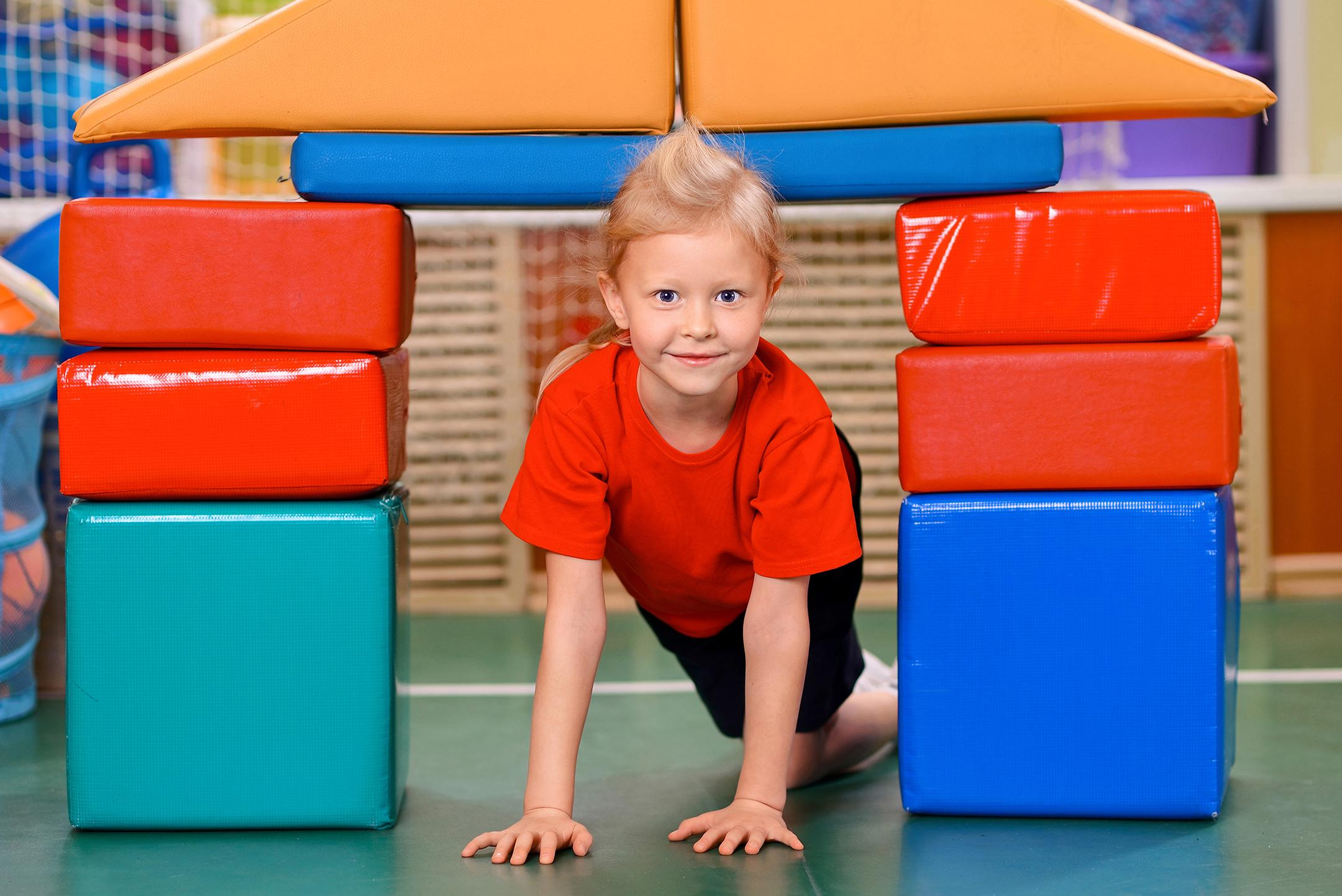 На физкультуре в детском саду ребенок проползает через ворота