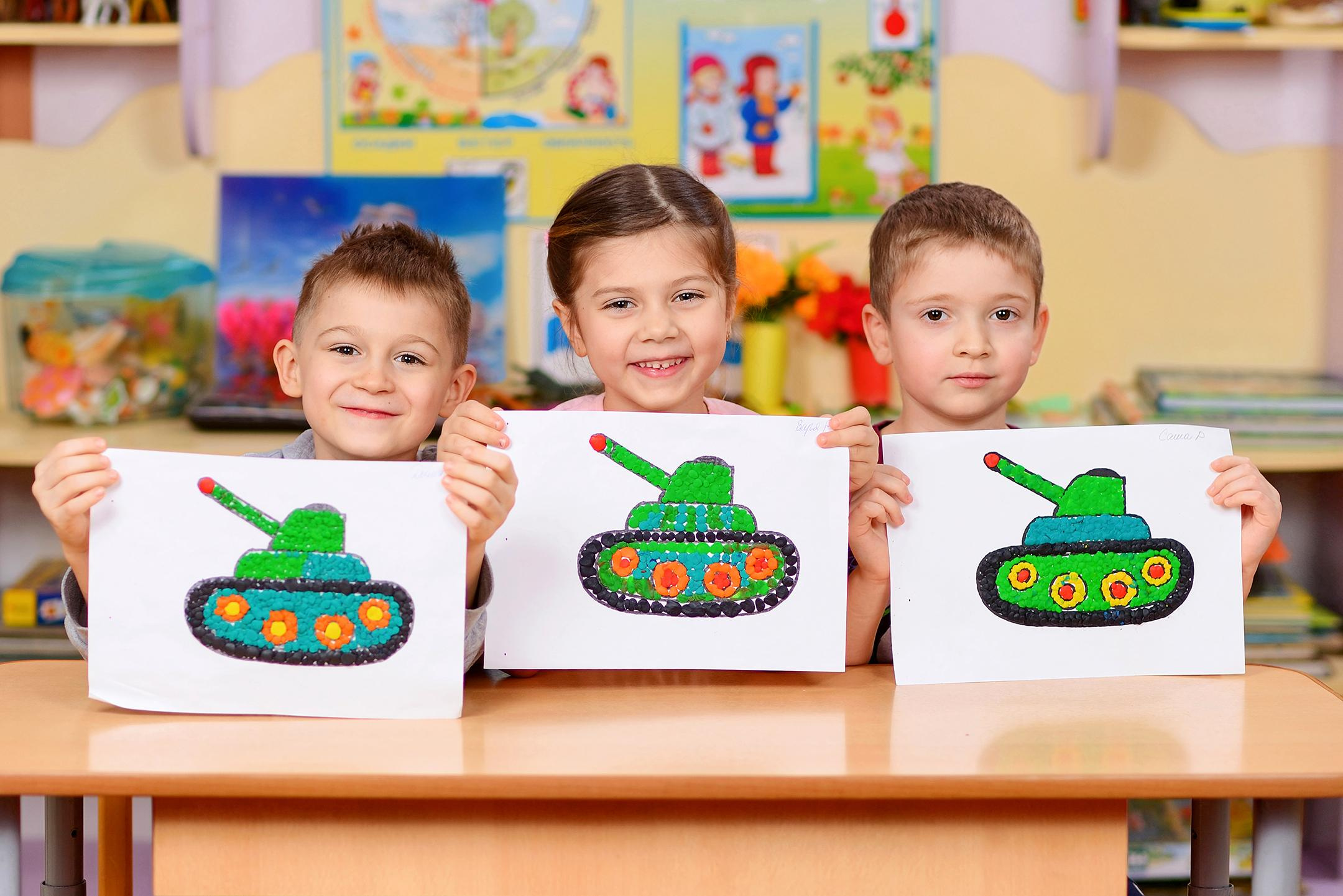 Дети в детском саду показывают свои рисунки из пластилина на тему войны