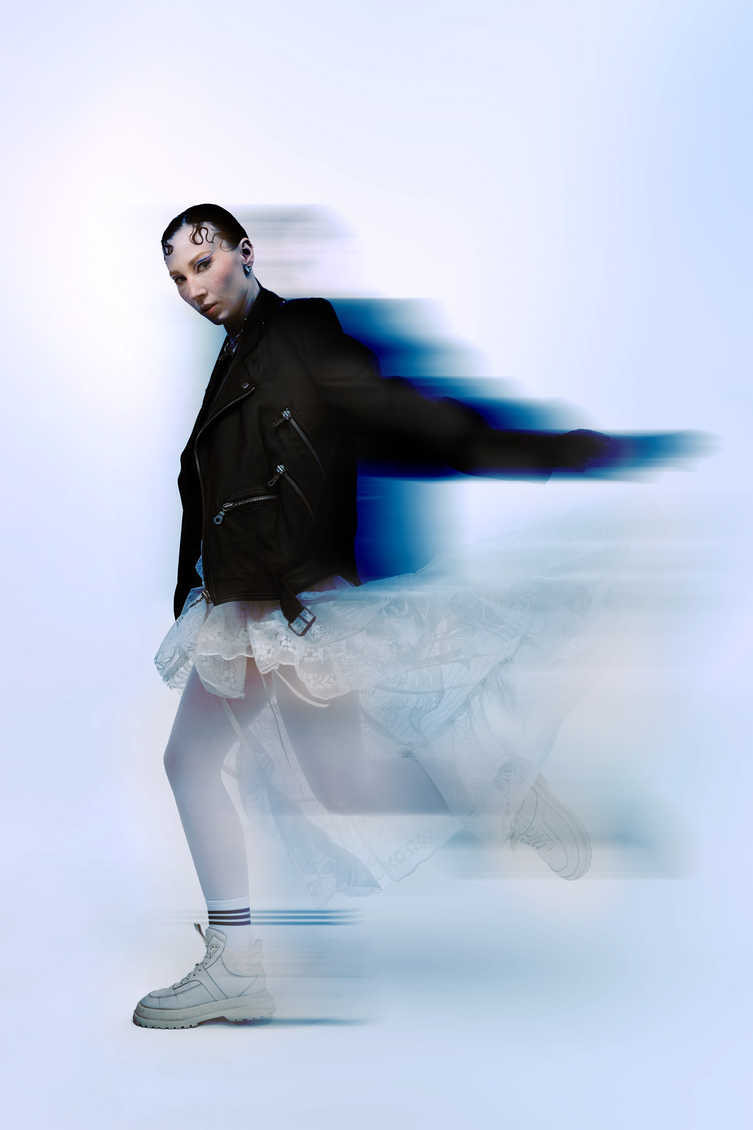 Танцовщица в черном пиджаке и пышной пачке демонстрирует динамичный прыжок, создавая завораживающее ощущение движения на безмятежном синем фоне.