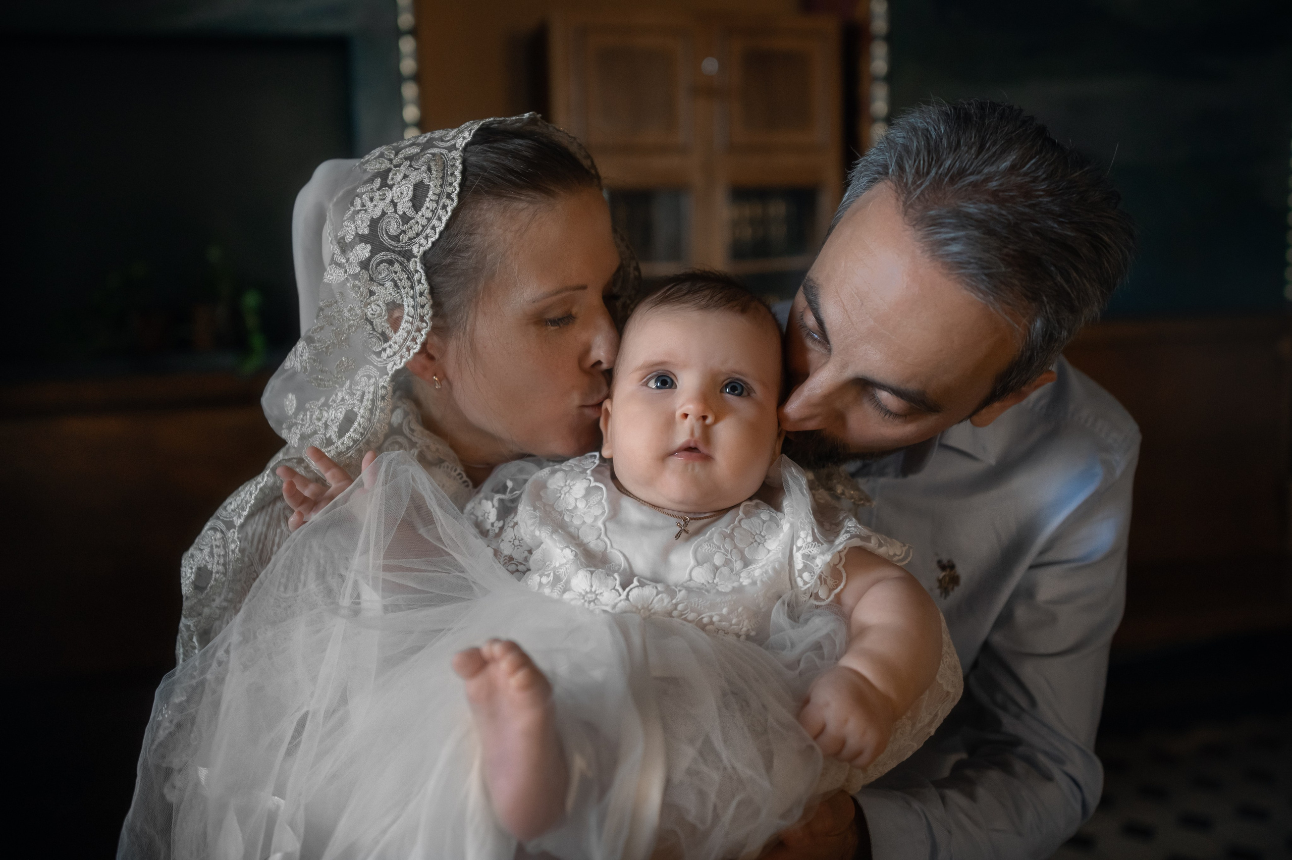 мама и папа целуют в щечки малышку на крещении в Успенском храме 