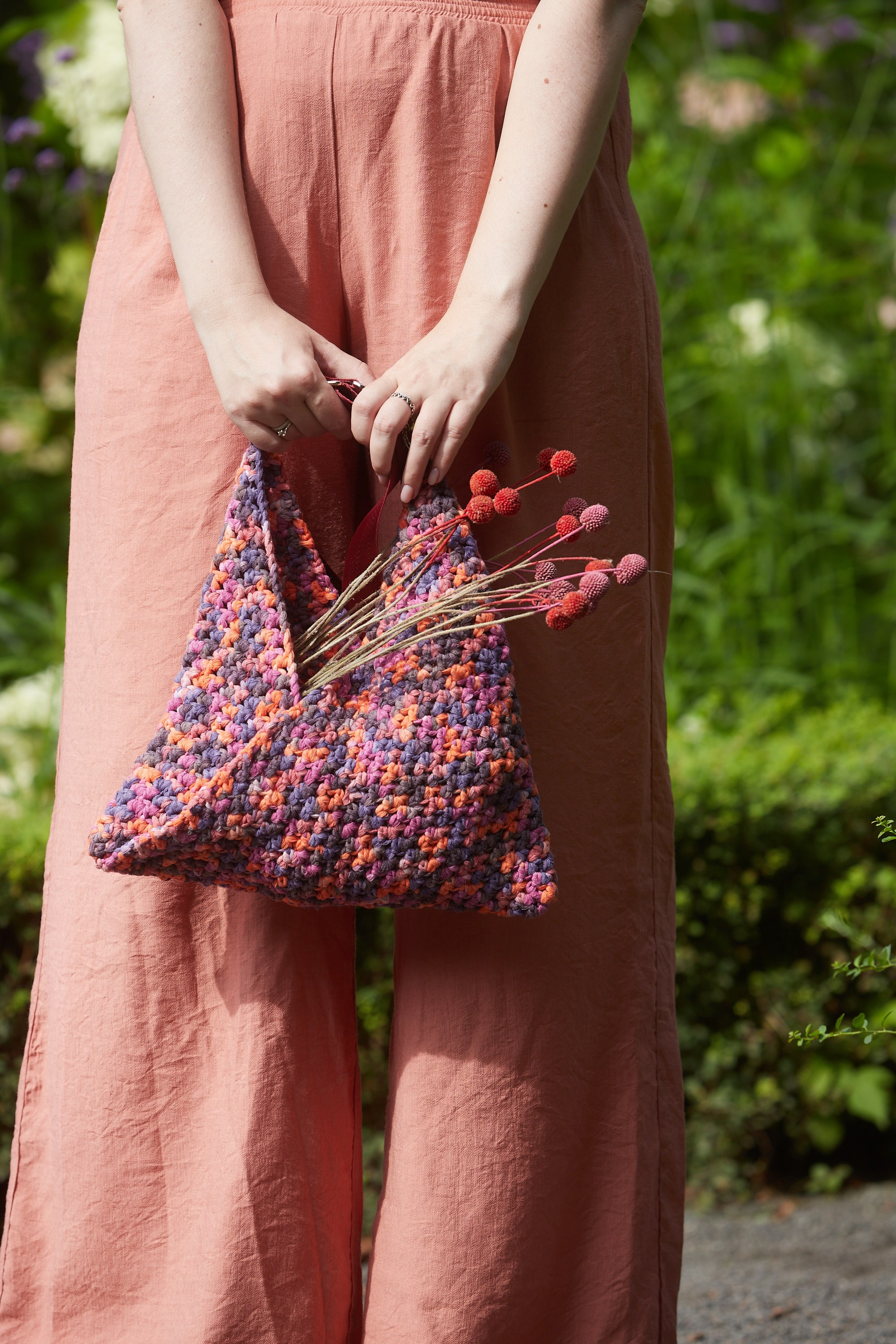 Вязаный аксессуар крупным планом на фоне зелени.