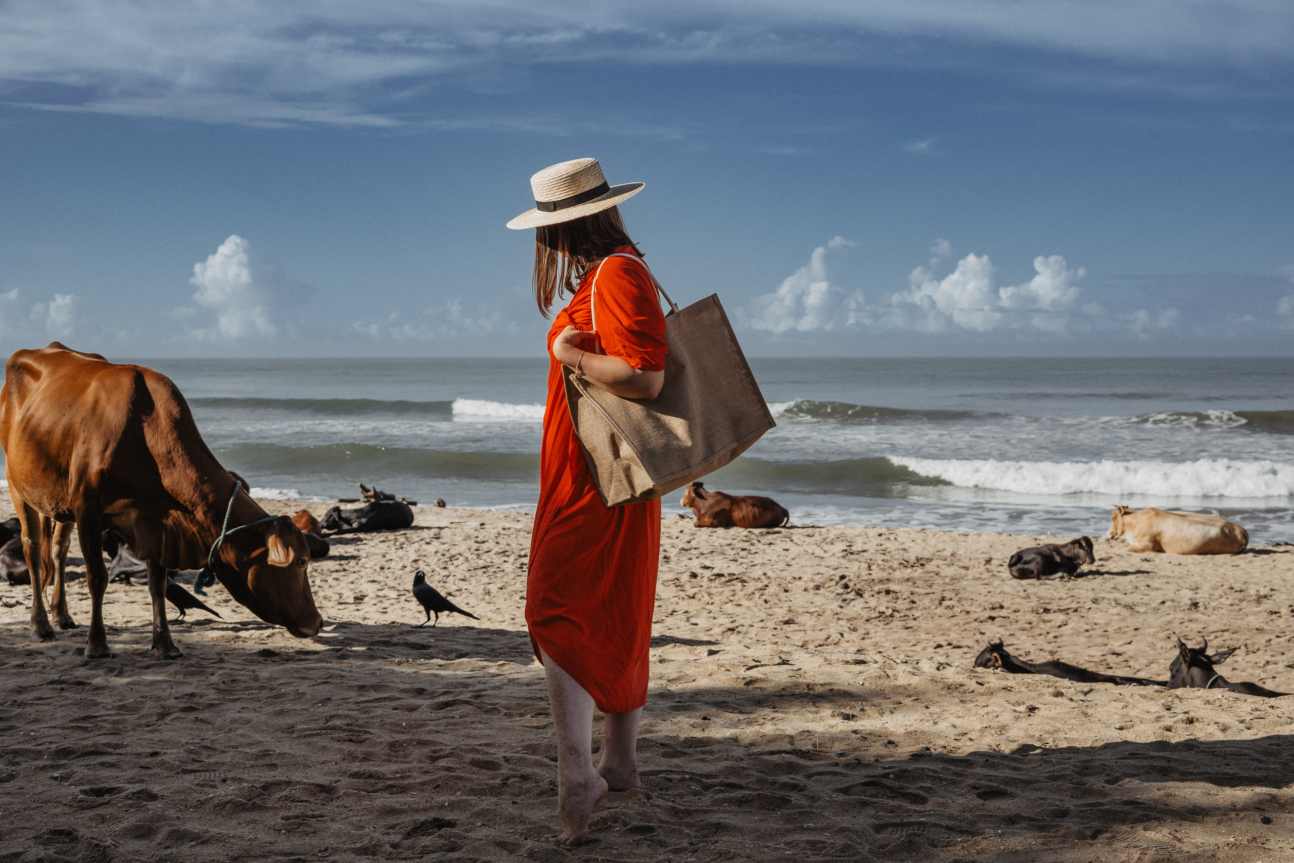 a girl in a straw hat taking photos with the beach and ocean in the background