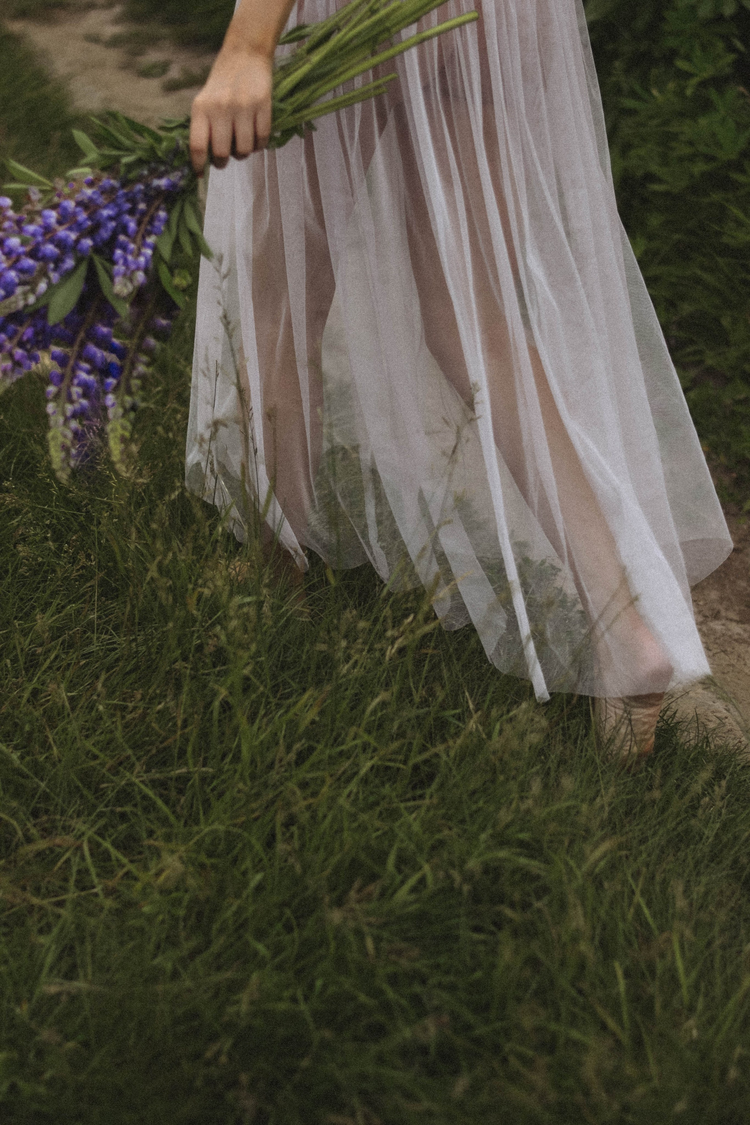 Девушка в белом платье держит букет люпинов.