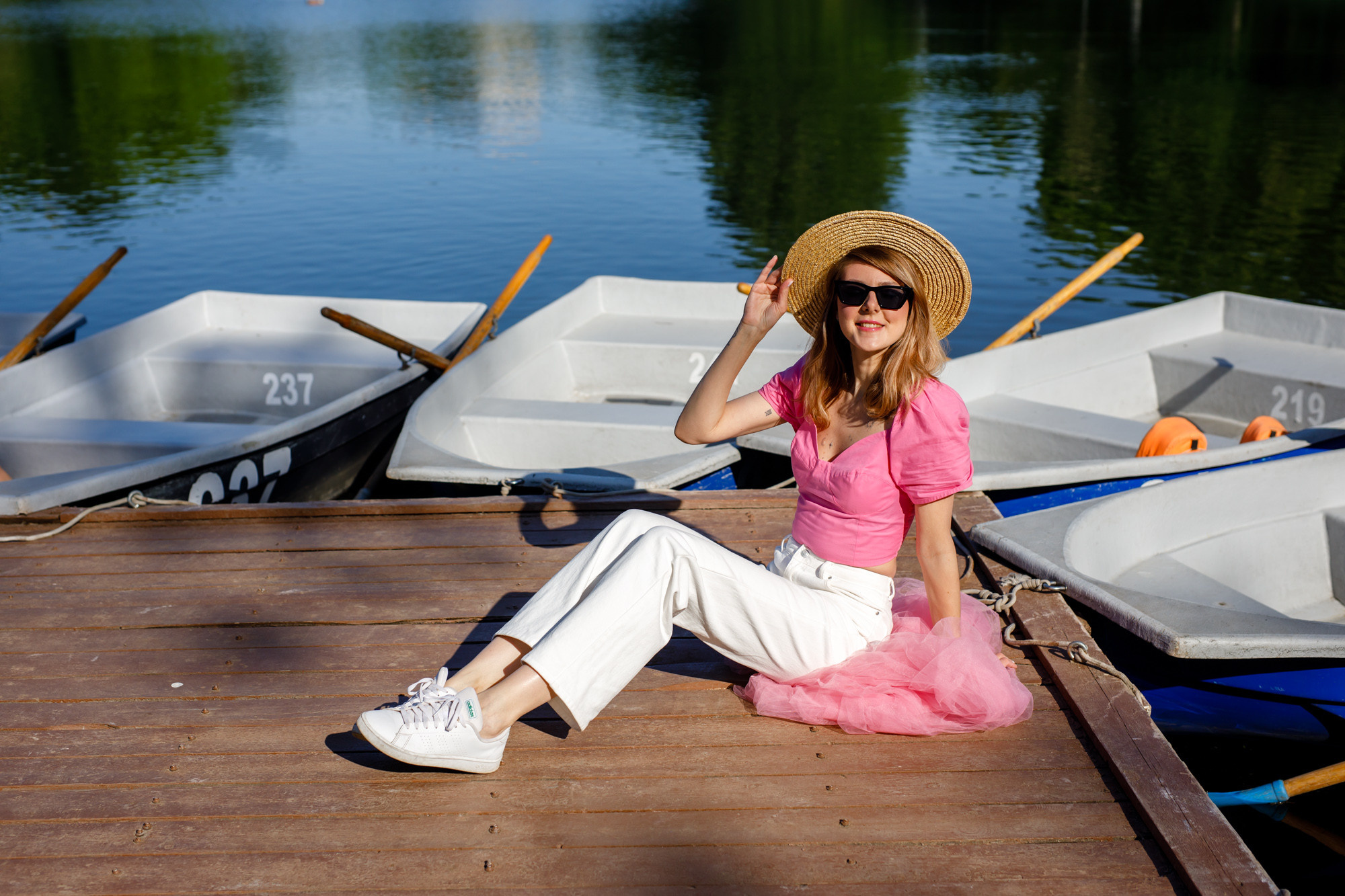 девушка у лодочного причала в розовом топе и белых джинсах в соломенной шляпке