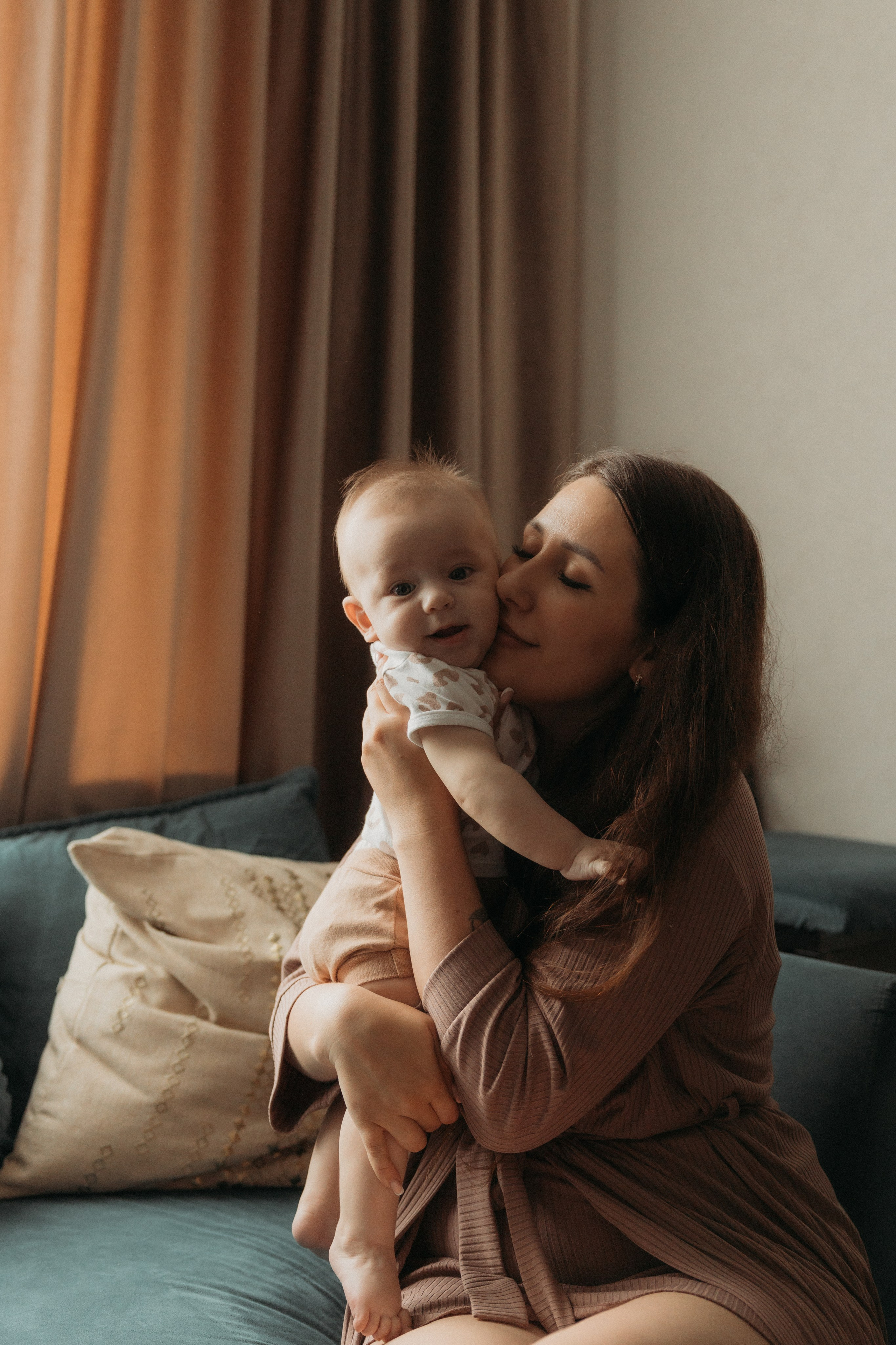 Мама целует малыша на руках во время фотосессии