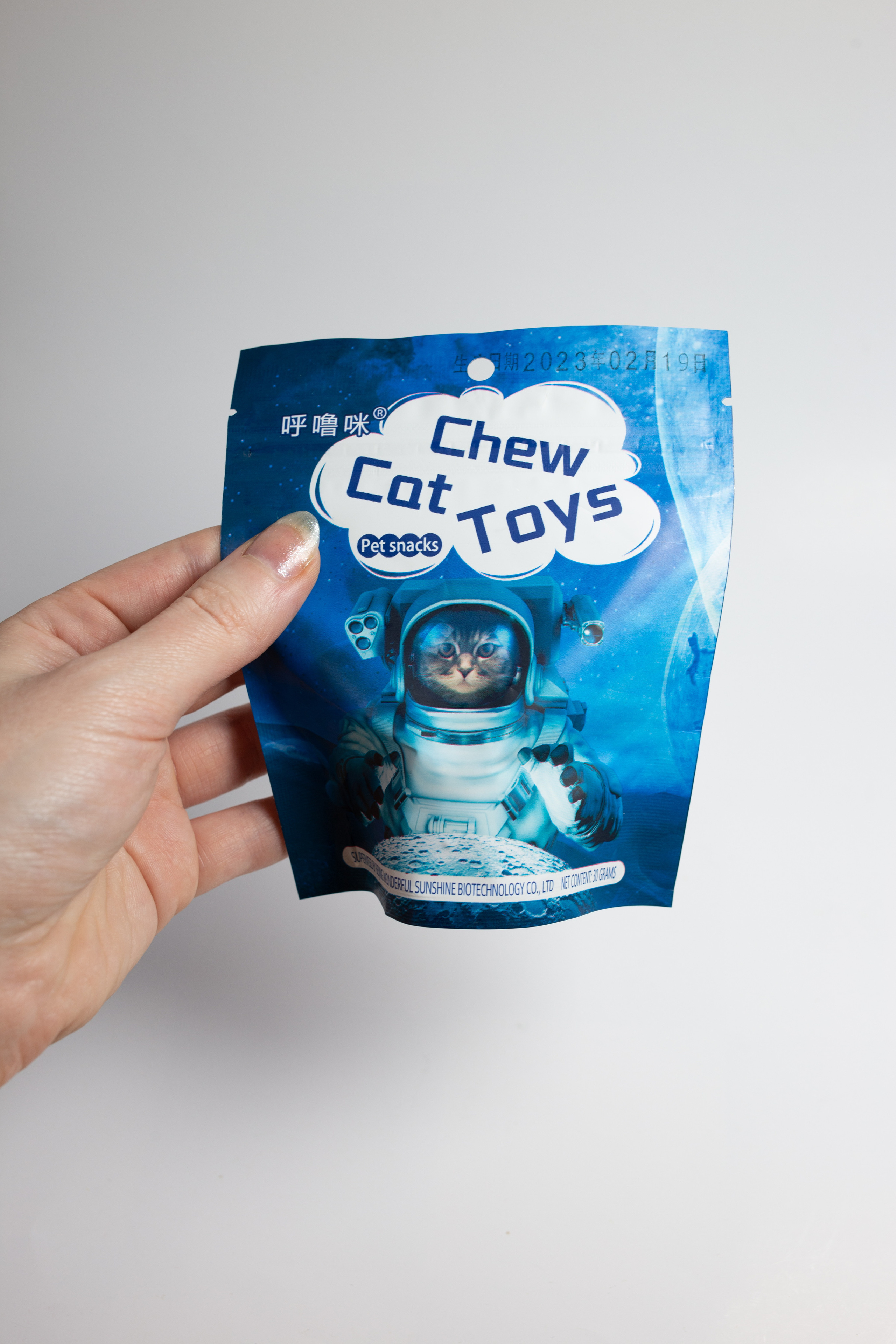 рука держит  упаковку  от   шарика  кошачьей мяты. рисунок  котик  космонавт. 