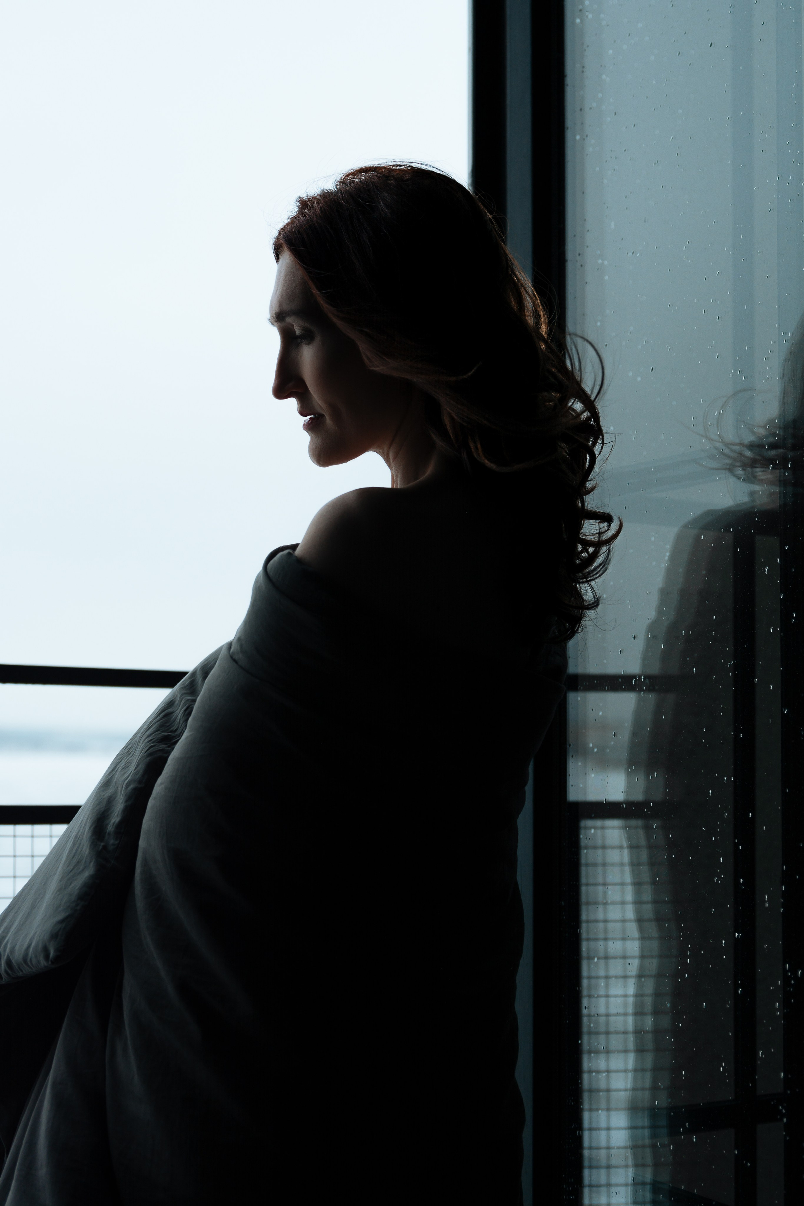 Девушка стоит у распахнутого окна, из которого доносится свежий ночной воздух. Ее стройная фигура укутана в мягкое одеяло, небрежно обернутое вокруг тела. 