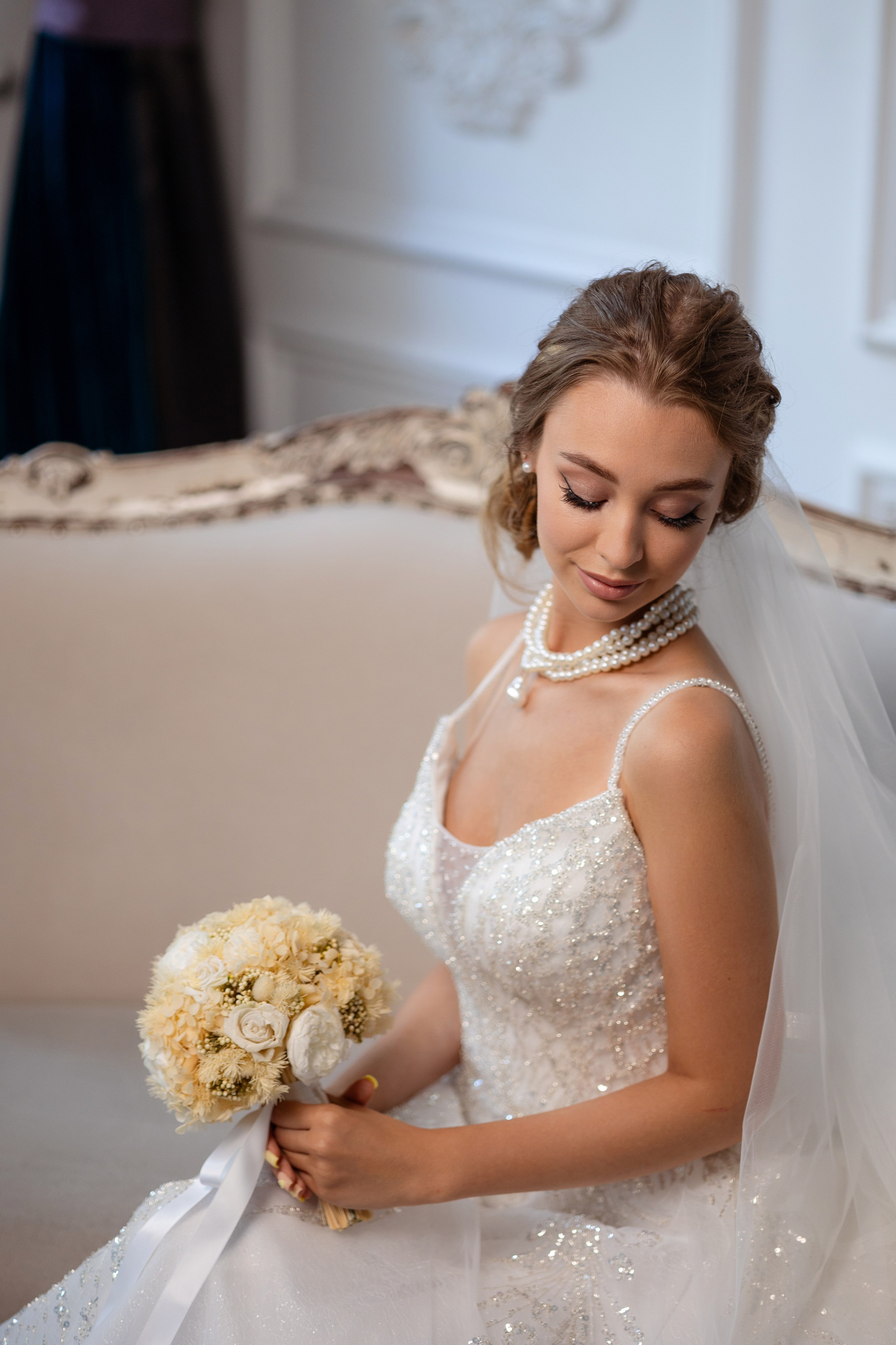 Невеста сидит со свадебным букетом в руках.