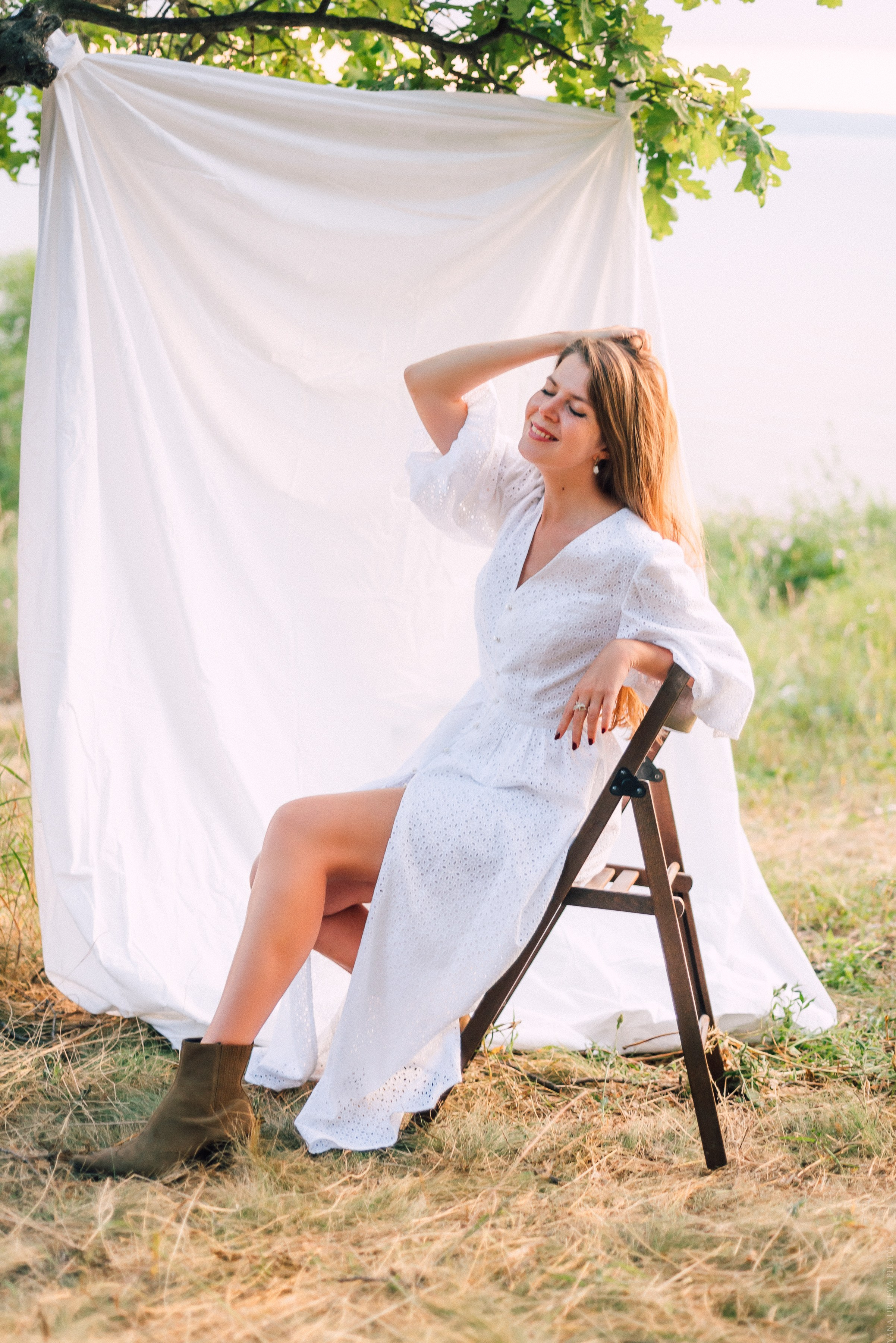 Девушка в белом легком летнем платье на фоне белой ткани в лесу