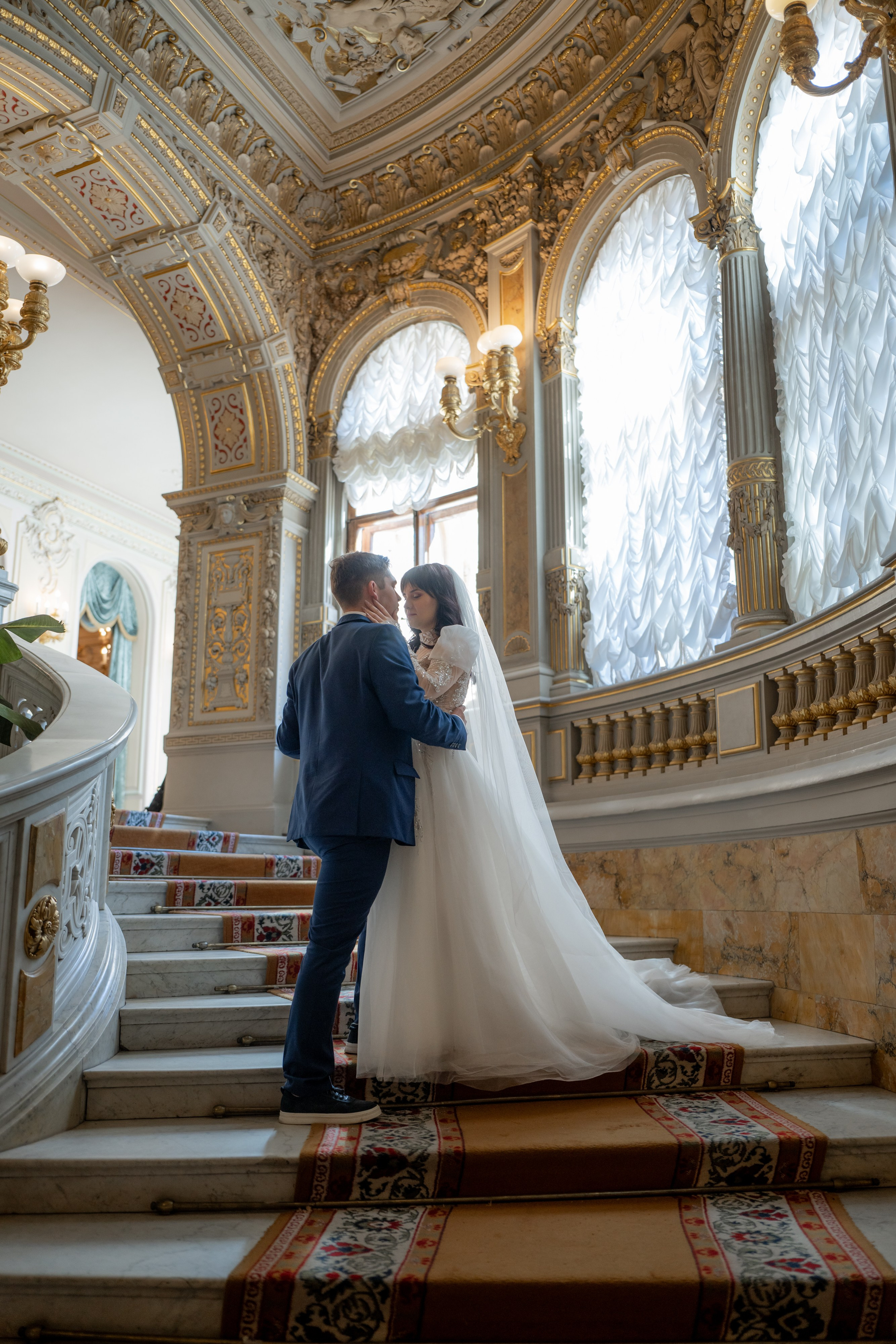 Свадебная фотосессия в Доме ученых, Дворце князя Владимира в Санкт-Петербурге. Жених с невестой обнимаются на парадной лестнице в контровом свете.