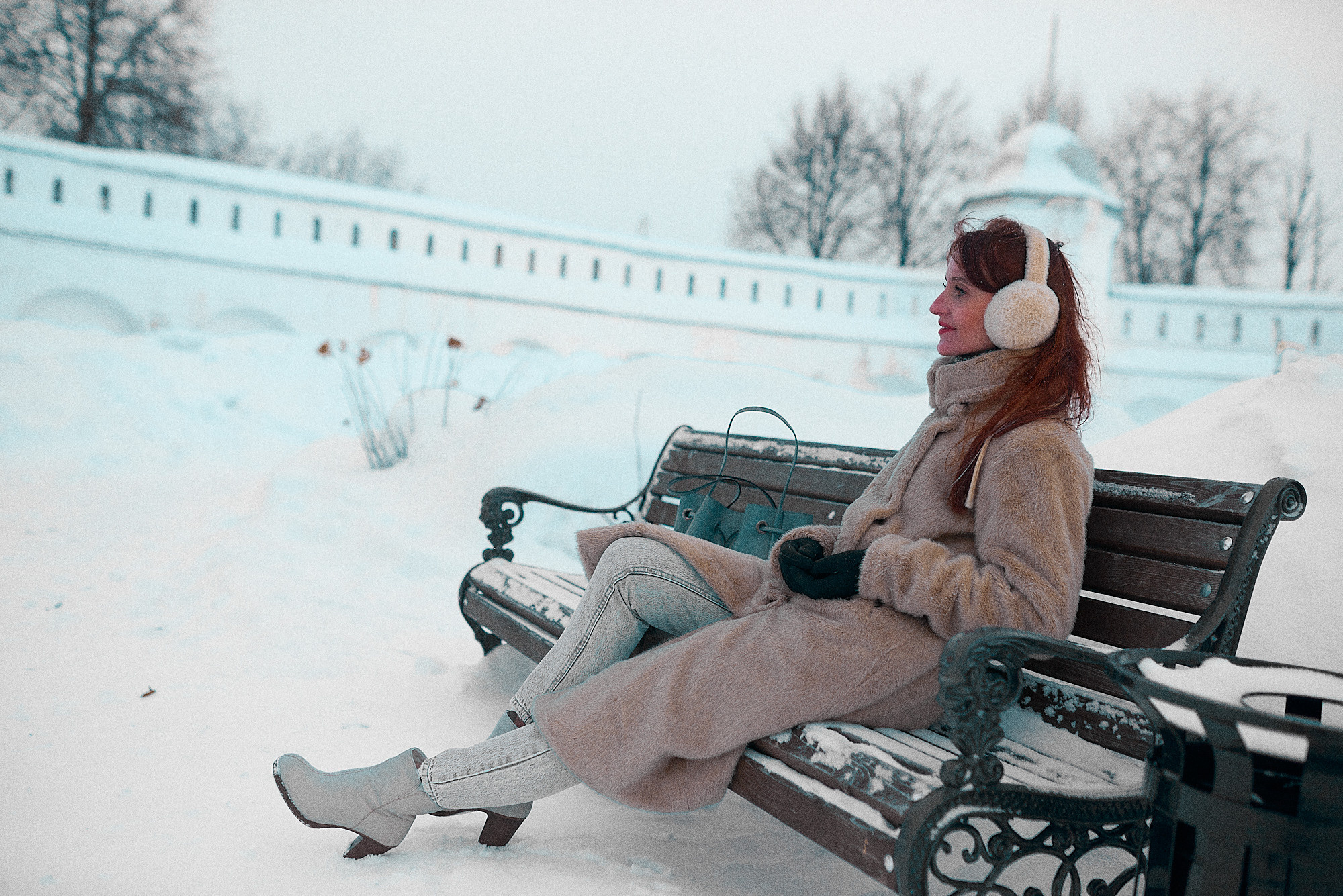 Молодая девушка отдыхает в зимнем парке на изящной скамейке