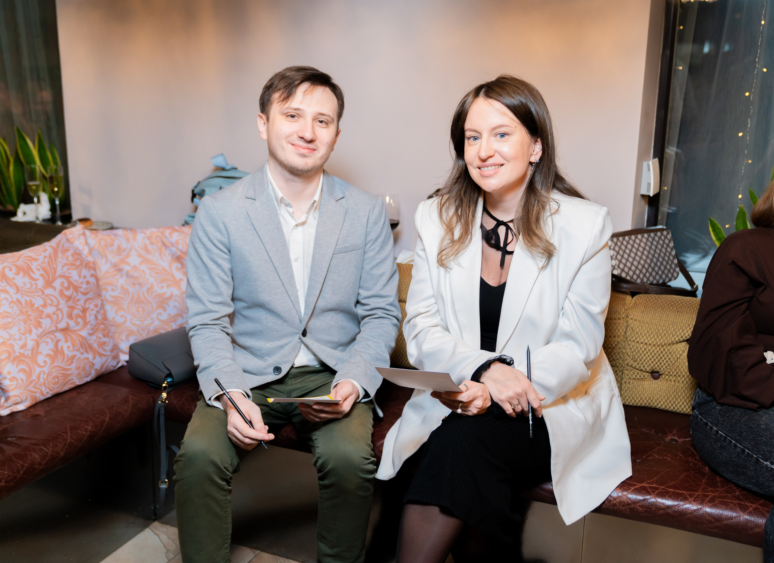 "Молодой мужчина в сером пиджаке и девушка в белом блейзере сидят на диване на мероприятии в Radisson Sonya. Фото Евгения Мальцева.
