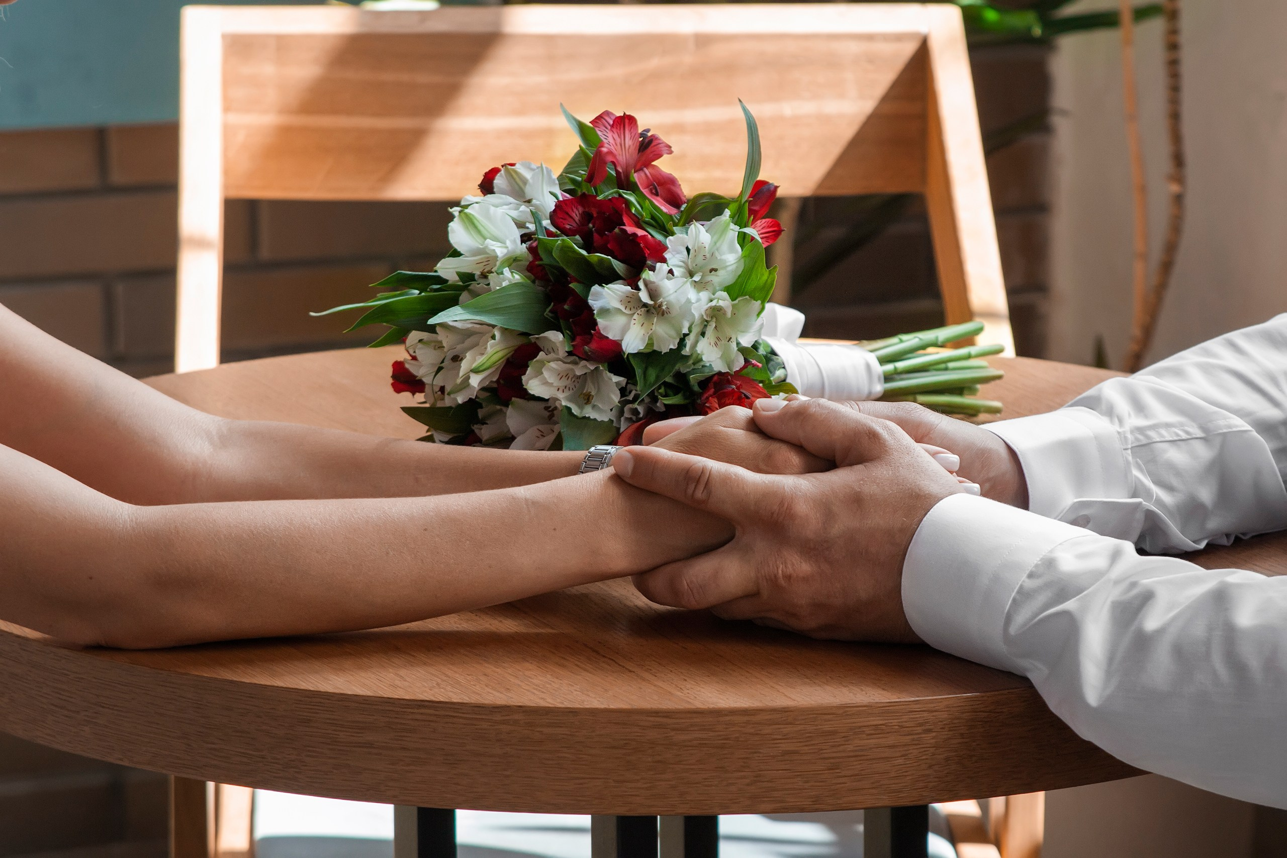 Руки жениха и невесты крупным планом на фоне свадебного букета